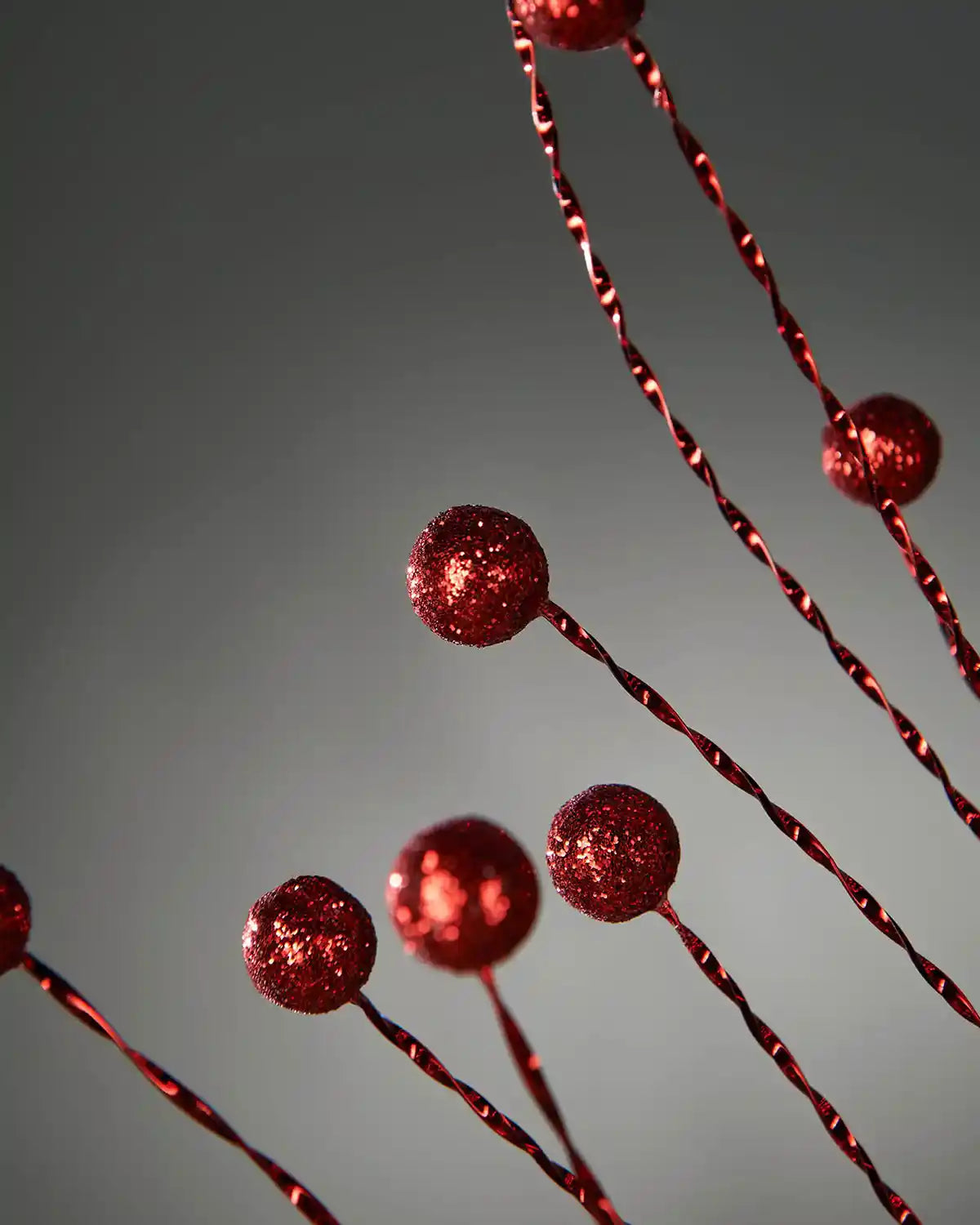 Close up of glitter Red berries on a Christmas tree spray on a grey background