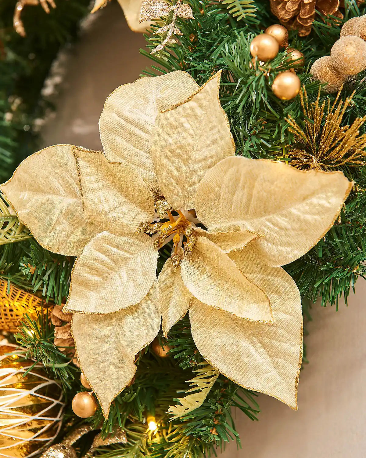 Close up of gold poinsettia flower on a Christmas tree with green leaves and gold ornaments.