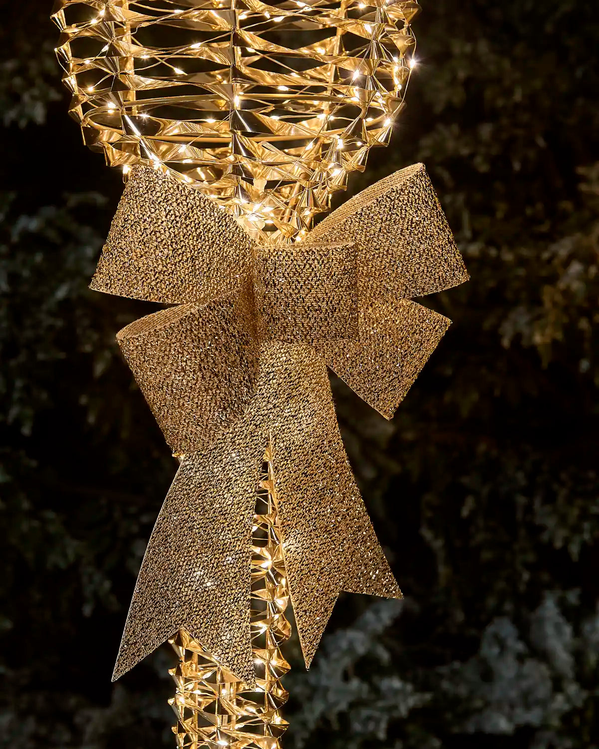Close up of golden bow on warm white and gold LED lamppost against a green foliage background