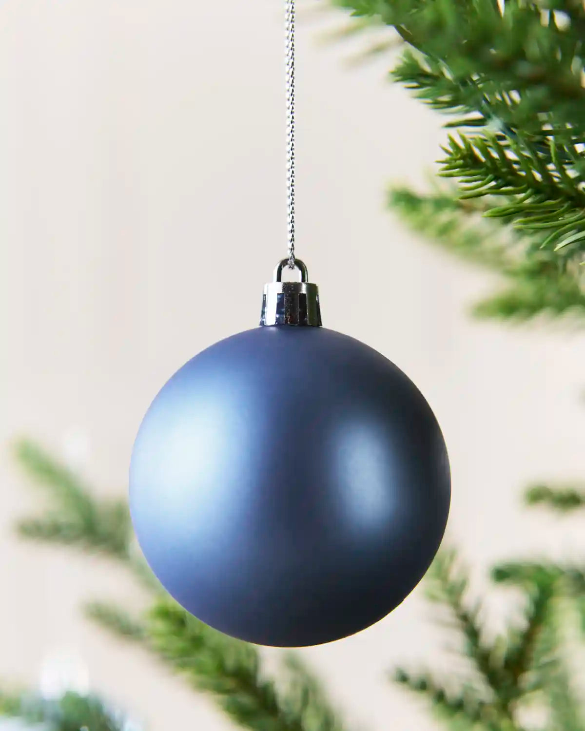 Close up of matt Ice blue Bauble hangingon a silver string on a Christmas tree against a blurry Cream background