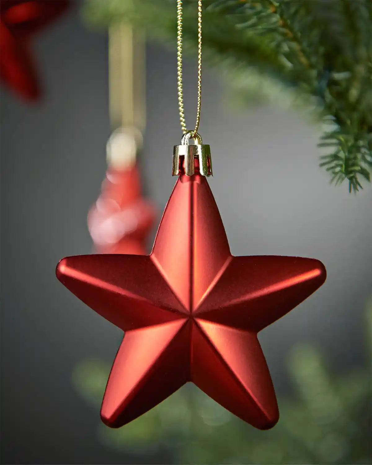 Close up of matt Star shaped hanging Christmas ornament against a blurry grey background