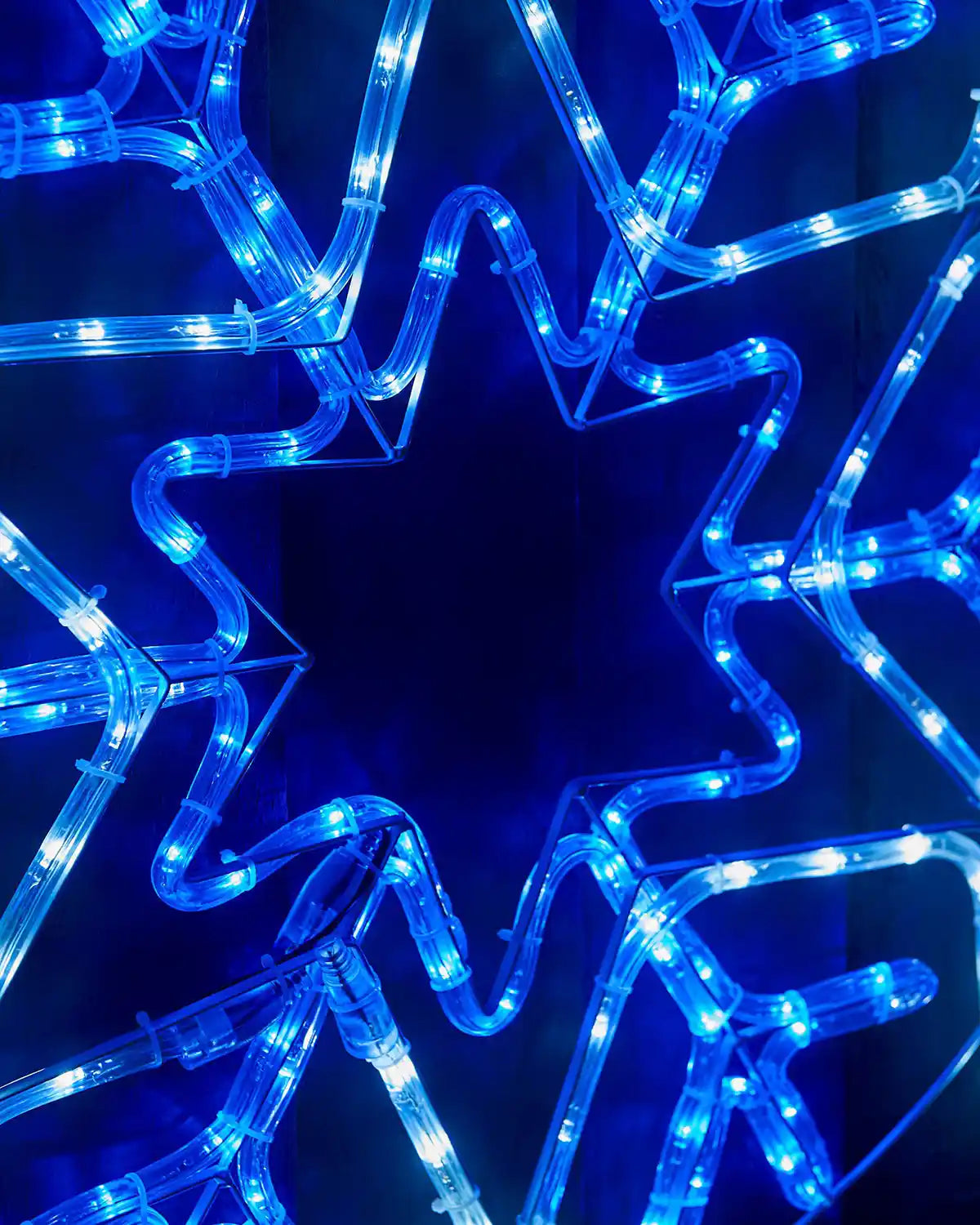Close up of middle of blue and white LED star in middle of snowflake on a fence  
