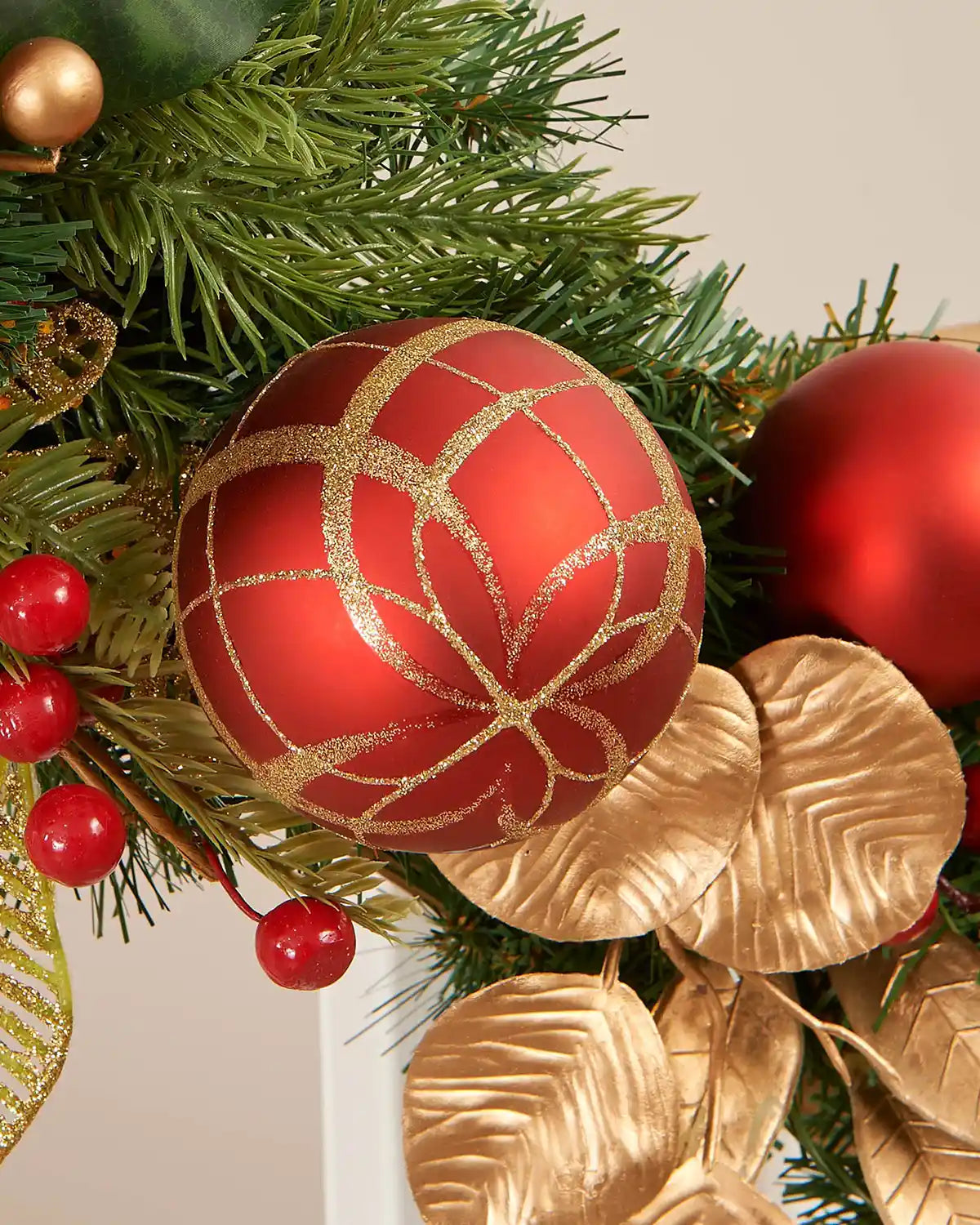 Close-up of green garland featuring red and gold decor, with red and gold bauble central to the picture, red and gold berries to the left, and gold foliage to the right