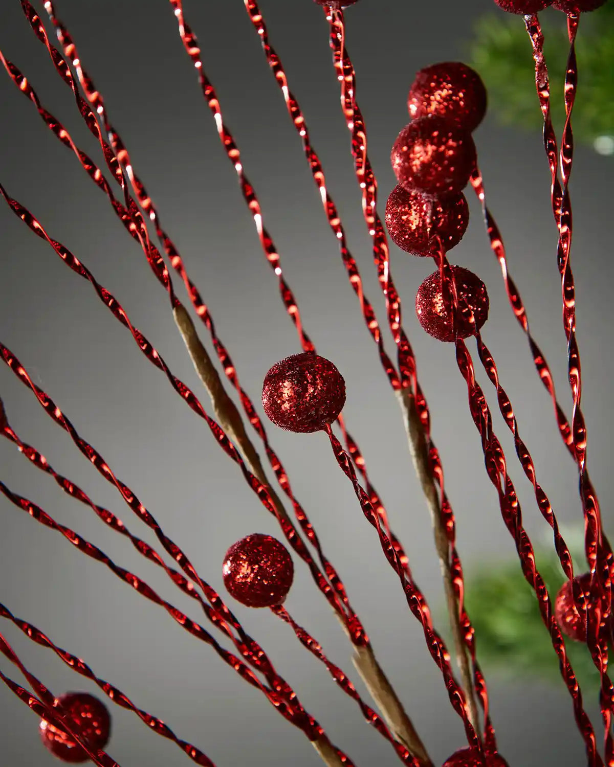 Close up of red glitter berry Christmas tree spray with a blurry Grey background