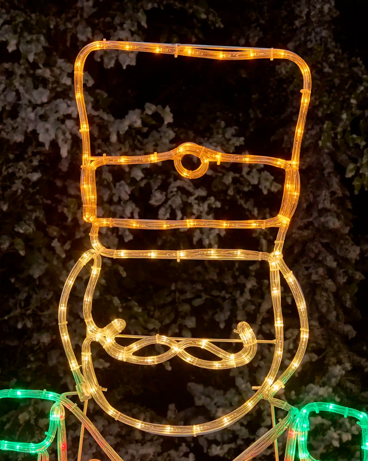 Close up of rope light nutcrackers hat and moustache against a snowy garden bush