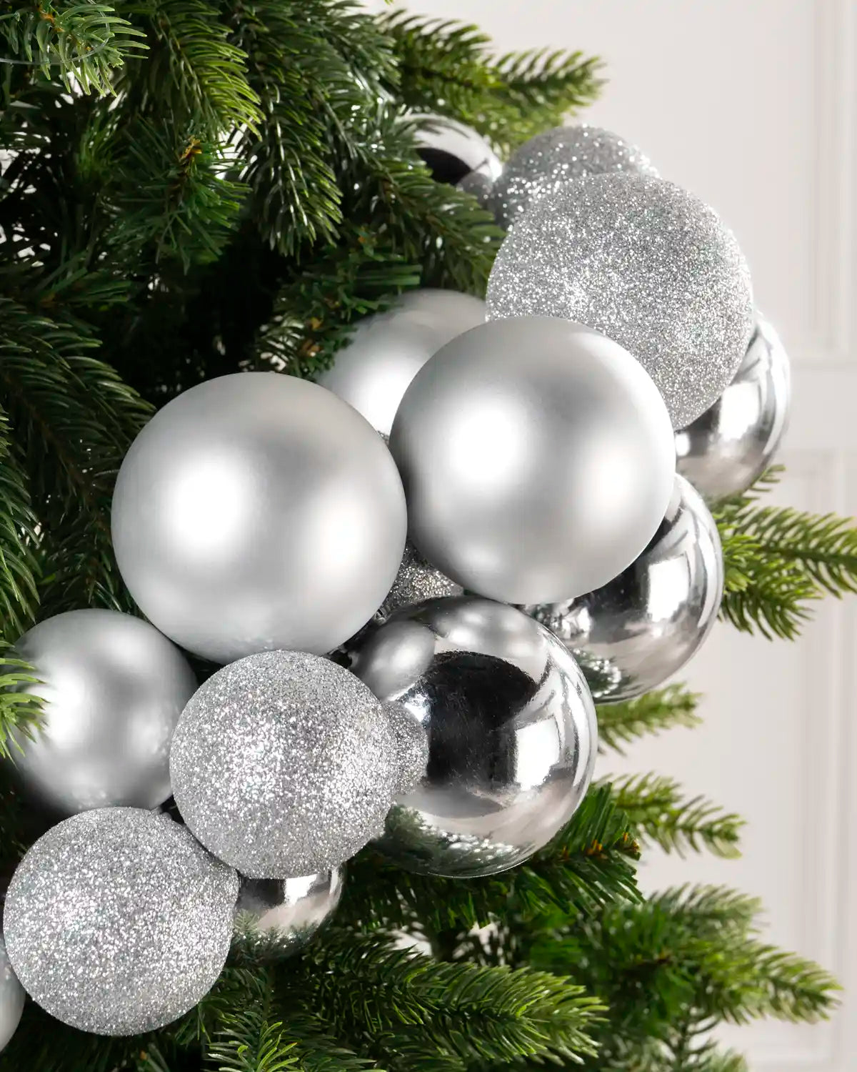 Close up of shiny silver and matte ornaments cluster bauble garland arch, shown against a plain light wall.