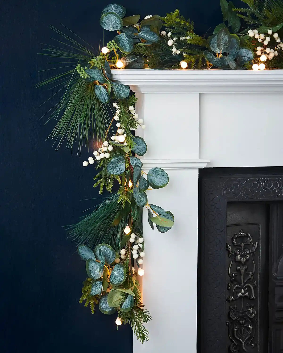 Close up of side of Decorative garland with Berries & Eucalyptuses, lights on a white fireplace mantel against a dark background