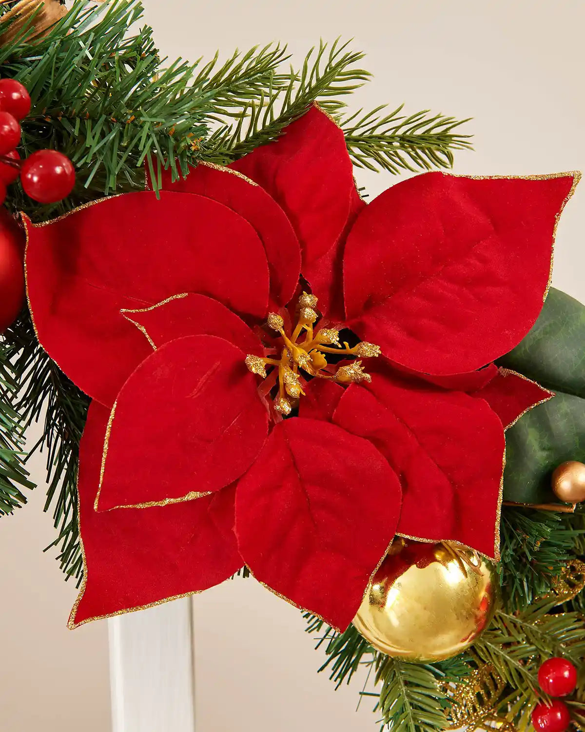 Close-up of green garland on white staircase banister highlighting the soft red fabric flower surrounded by red berries and gold baubles