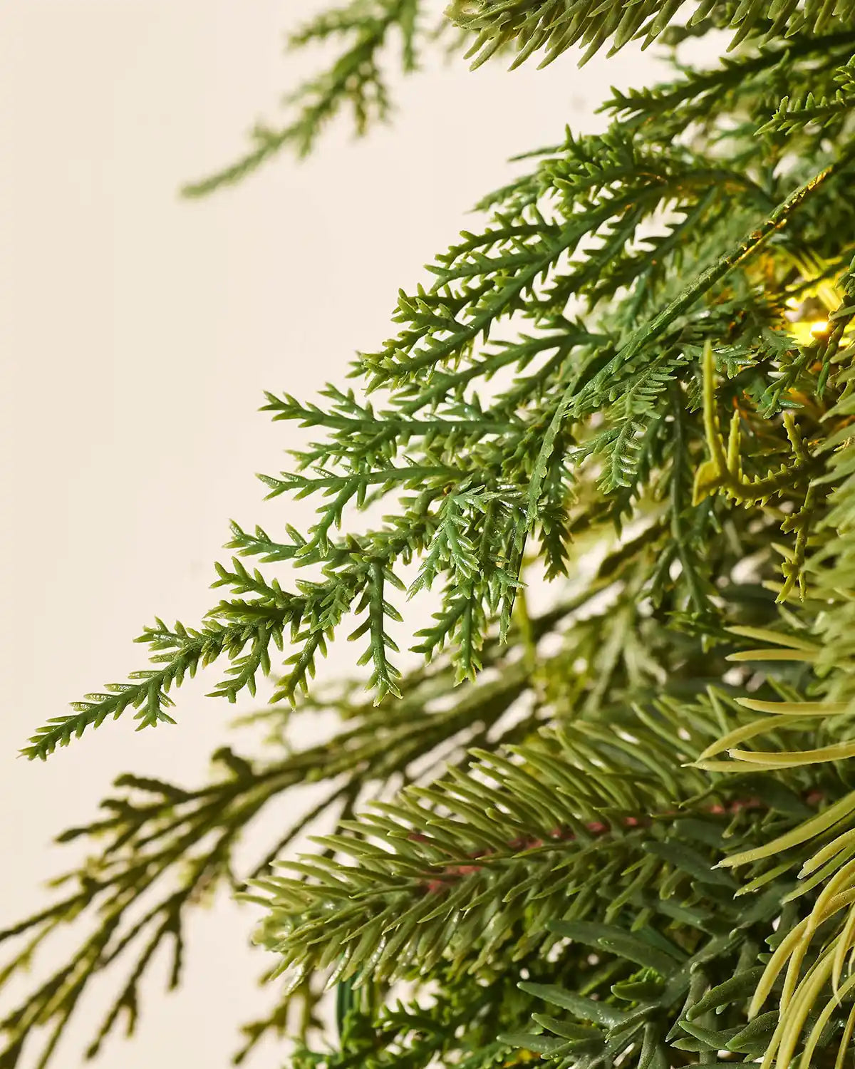 Close up of the PE tips and single lit Warm White bulbs of a Pre-Lit Natural Fir Majestic Wreath, 1.5 m on a cream background