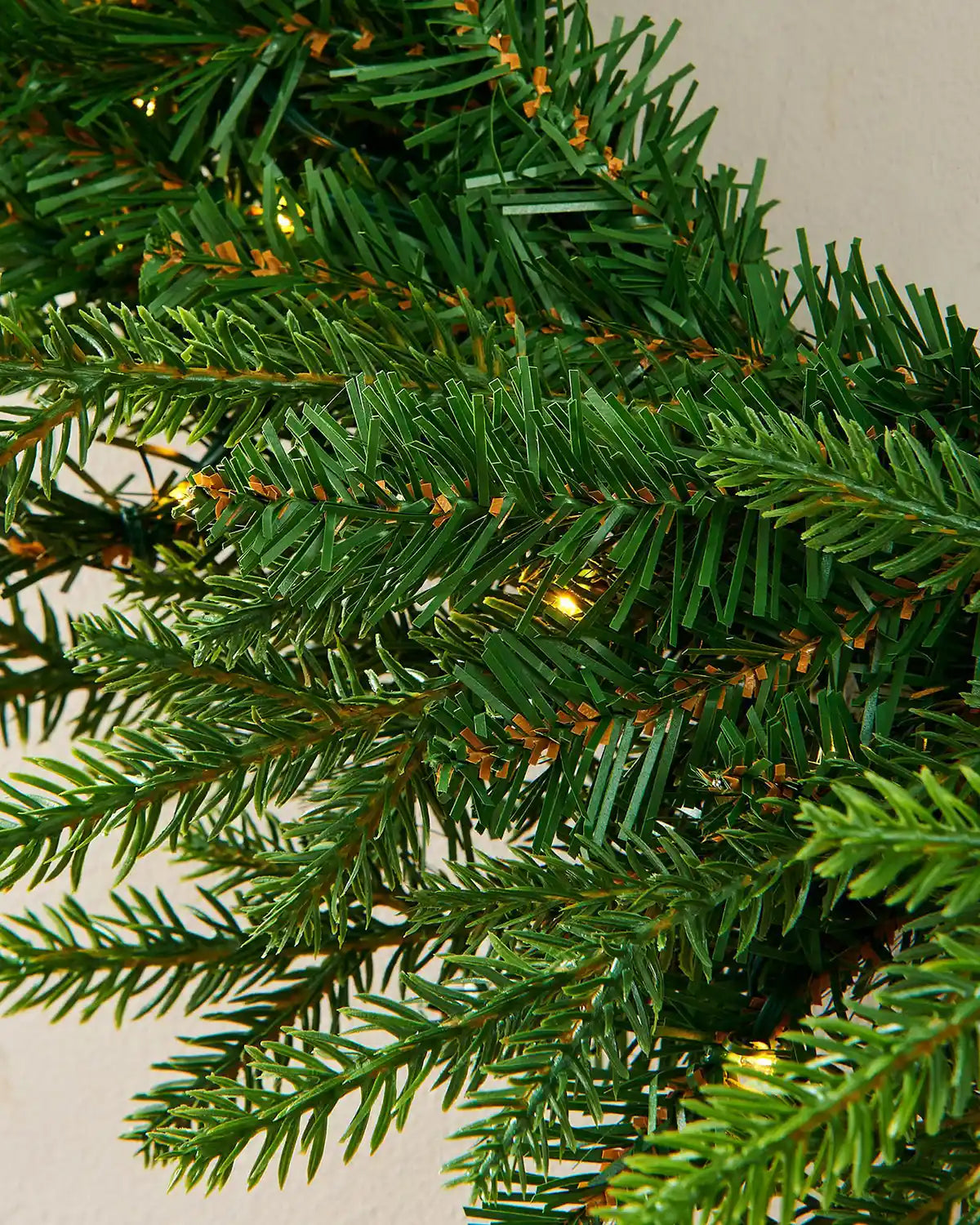 Close up of the PVC, PE tips and single lit bulbs of the Pre-Lit Multi-Function Douglas Fir Wreath, 60 cm on a cream wall