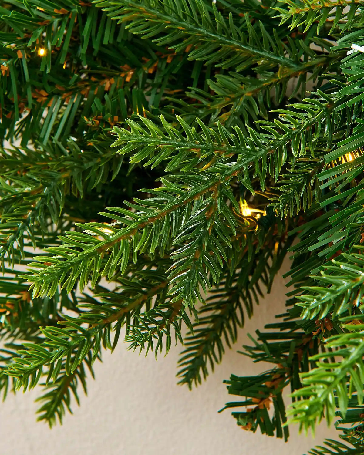 Close up of the PVC, PE tips and single lit bulbs of the Pre-Lit Multi-Function Douglas Fir Wreath, 60 cm on a cream wall
