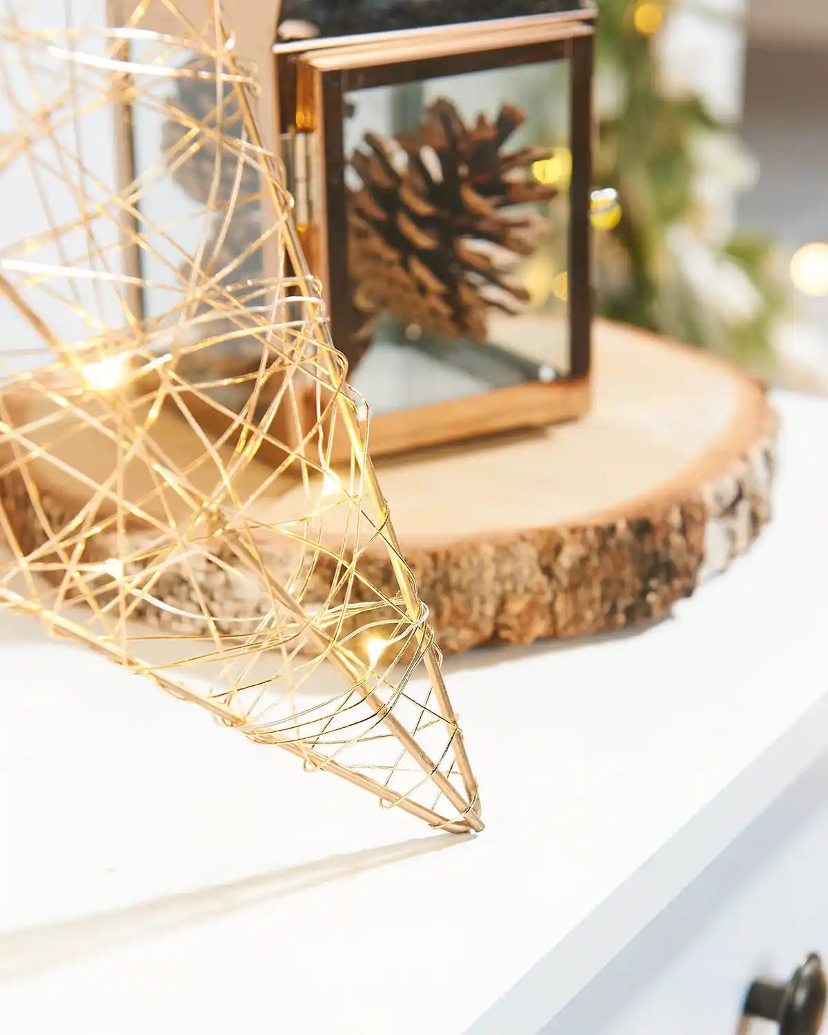 Close up of the bottom right point of the Pre-Lit 2D Metal Star, Gold with Pine cone Lantern in background 
