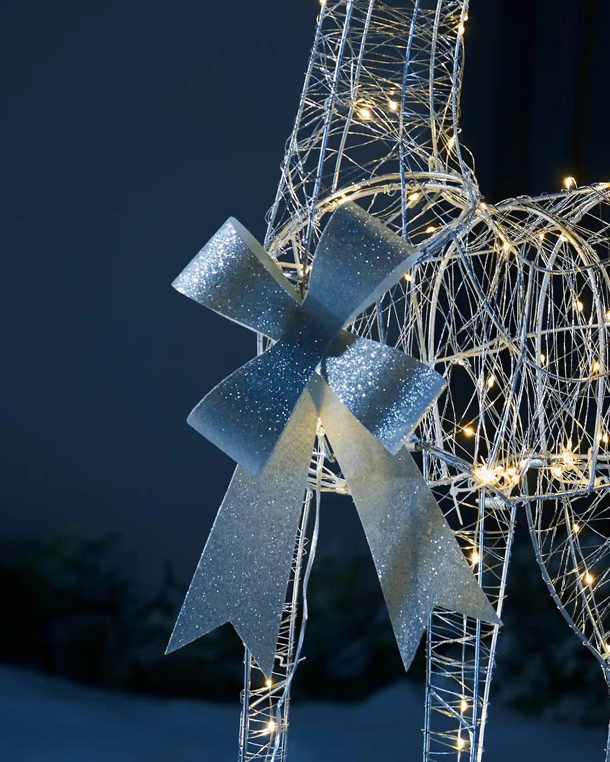 Close up of the calf's Glitter Silver bow  in a snowy garden at night time