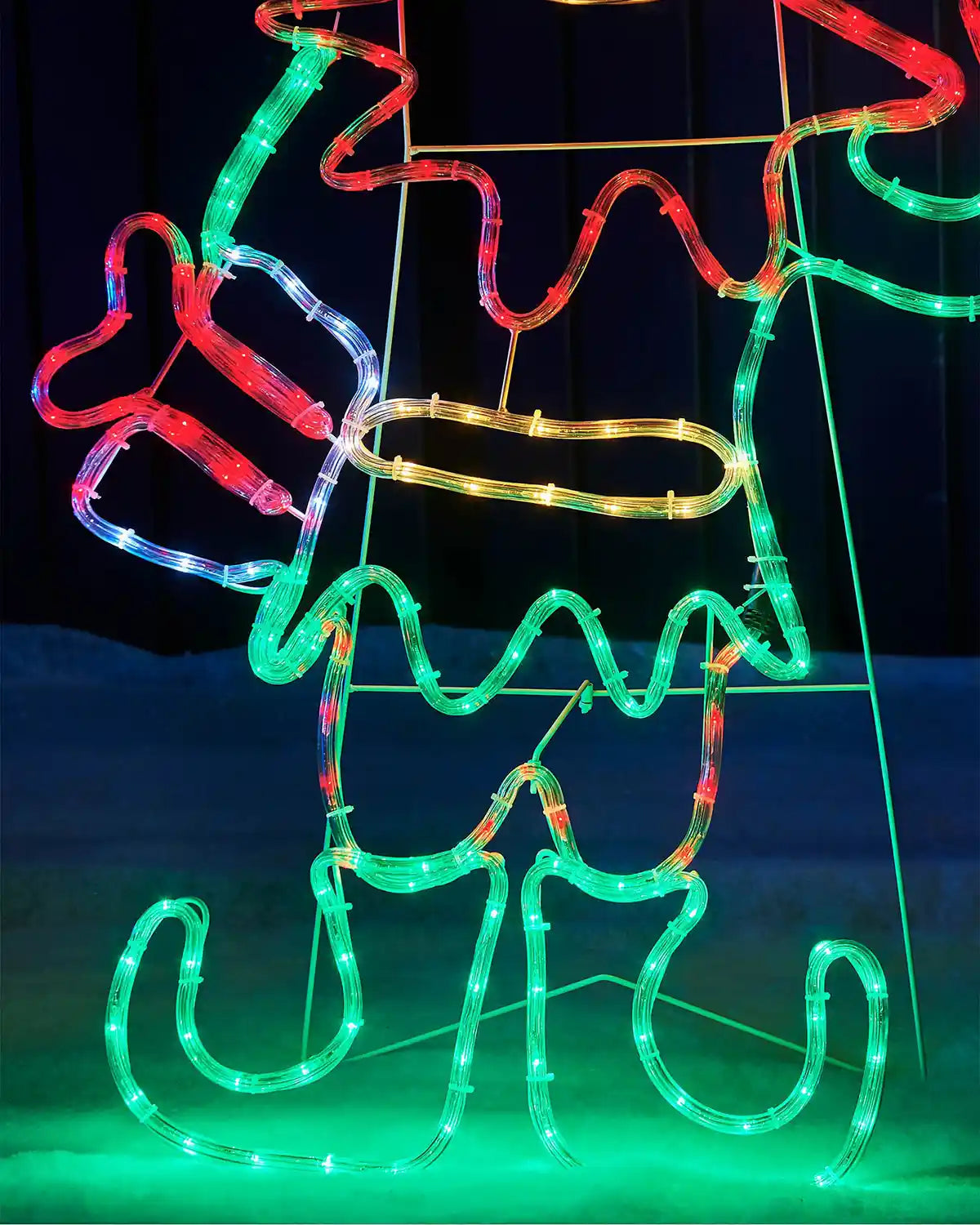 Close up of the elf's Green boots, red and white present on snowy grass and a dark fence 