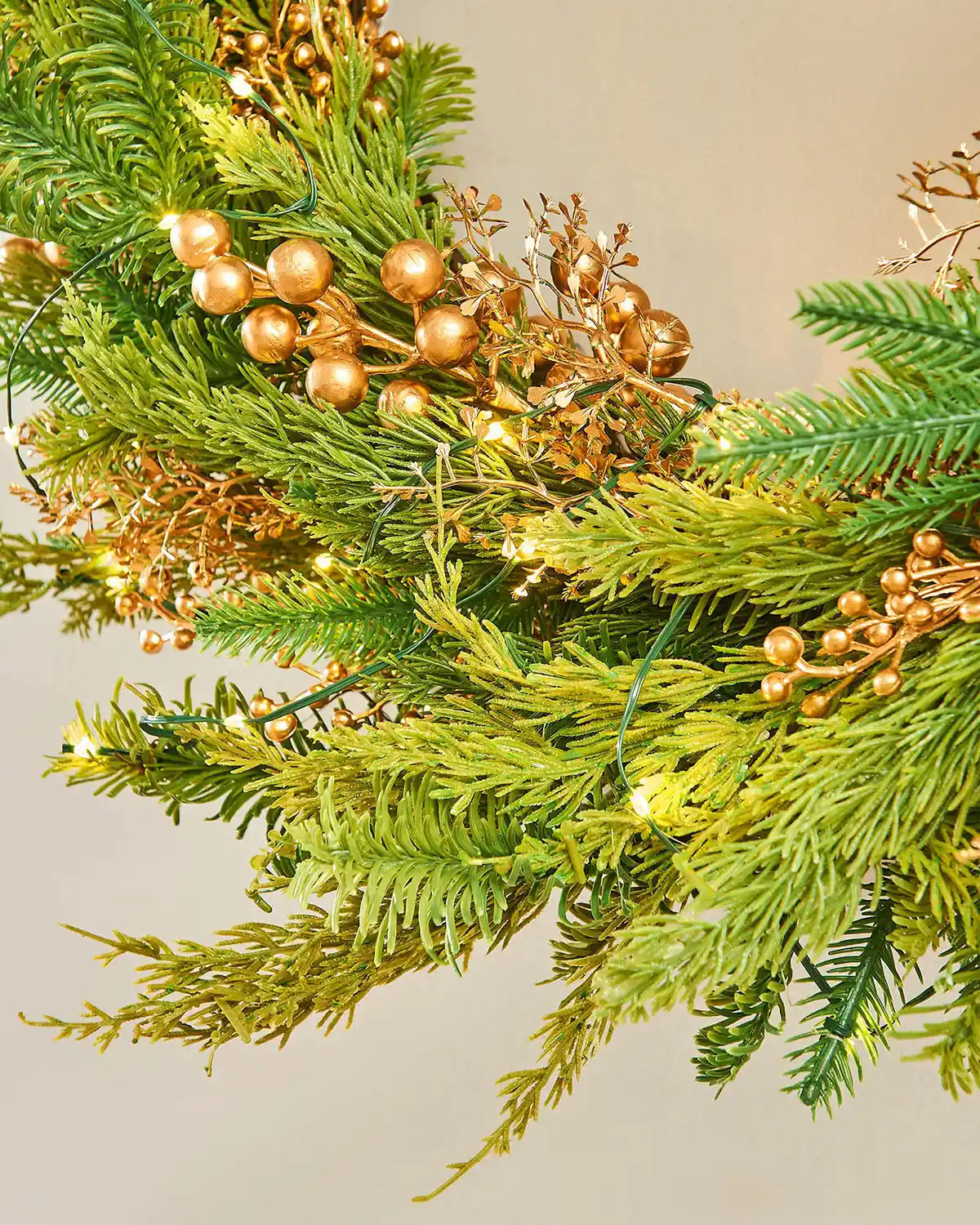 Close up of the tips on the decorative Gold Berry wreath with greenery and small lights on a white background