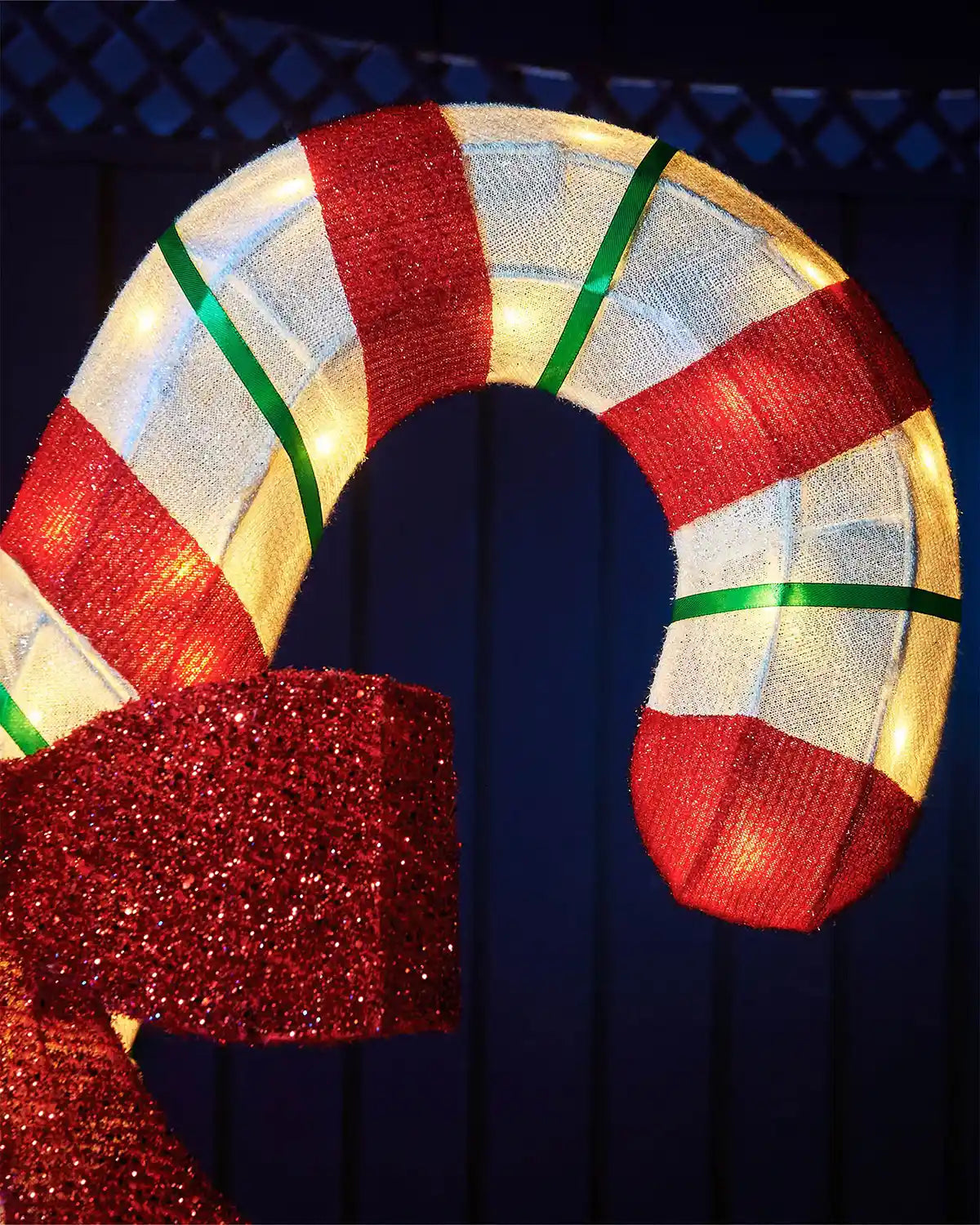 Close up of top of LED White and red candy cane with a bow on a dark background