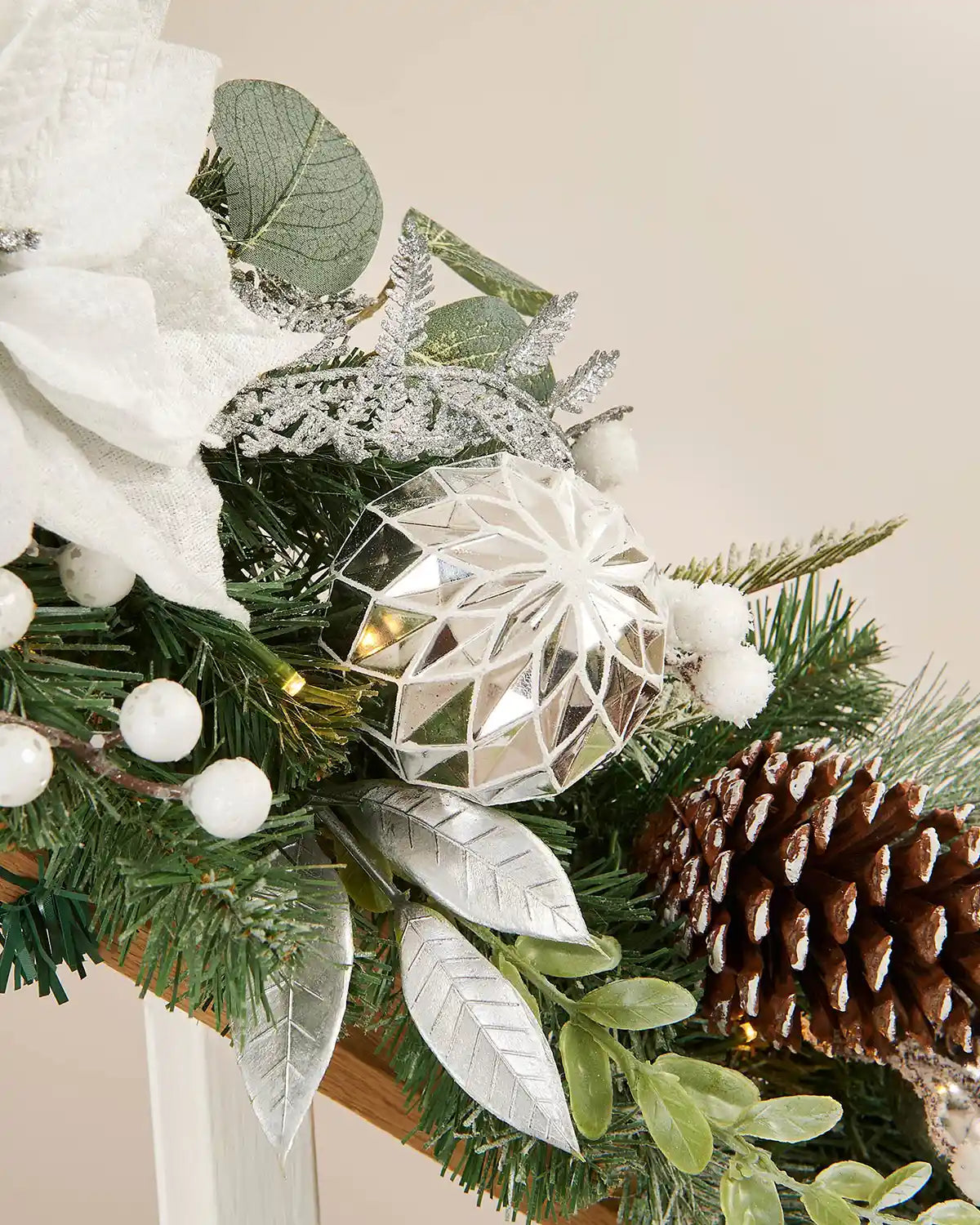 Close-up of silver and white garland on a wooden staircase with a focus on a silver bauble, snow-sprinkled pine cone and foliage