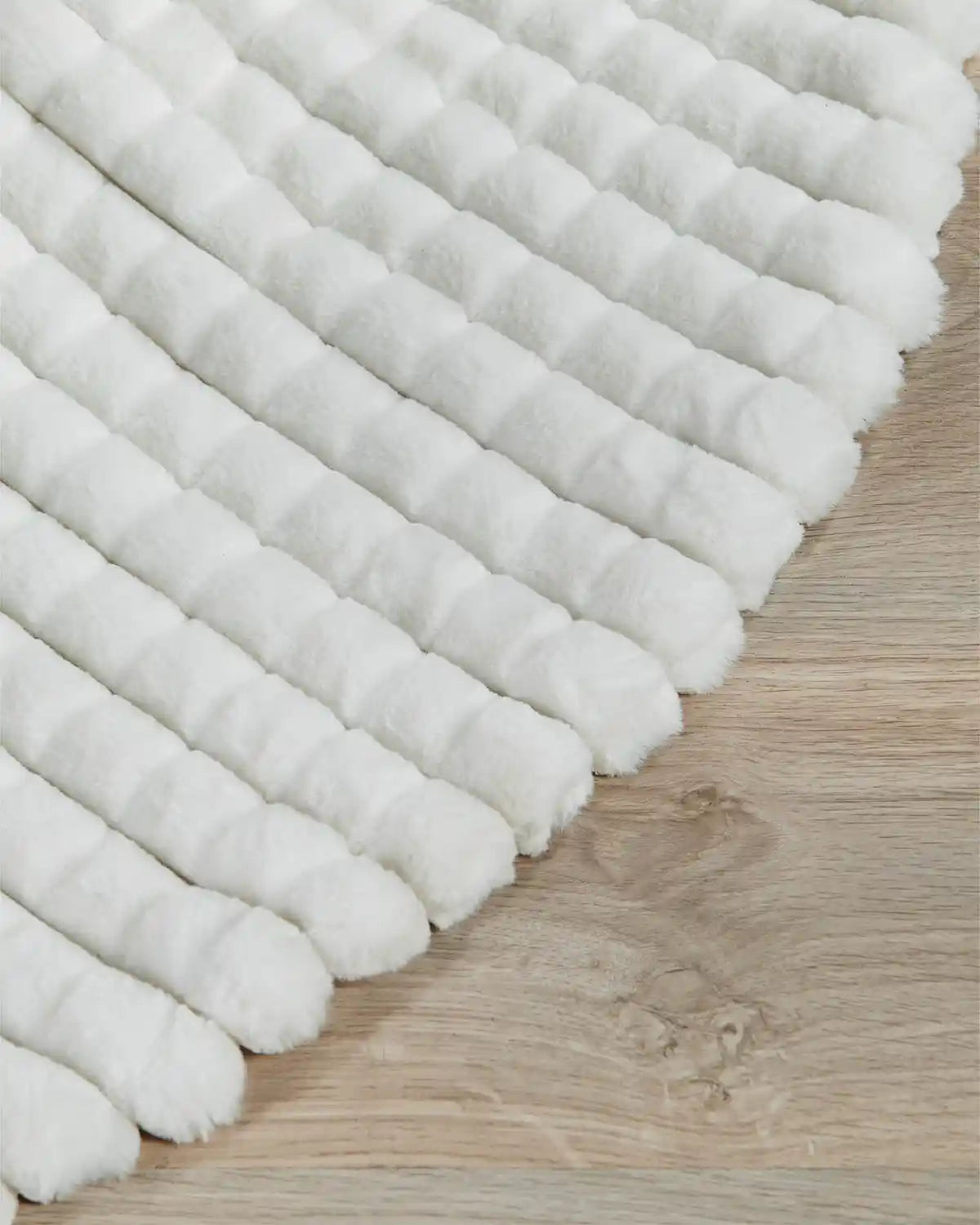 Close up of white faux fur diamond tree skirt edge on light wooden flooring, highlighting the softness of the material