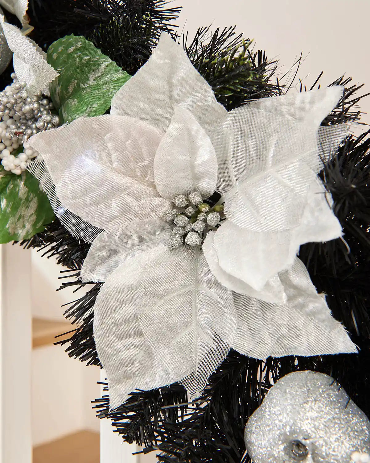 Close-up of white foliage on black garland surrounded by additional silver foliage on a white wooden staircase
