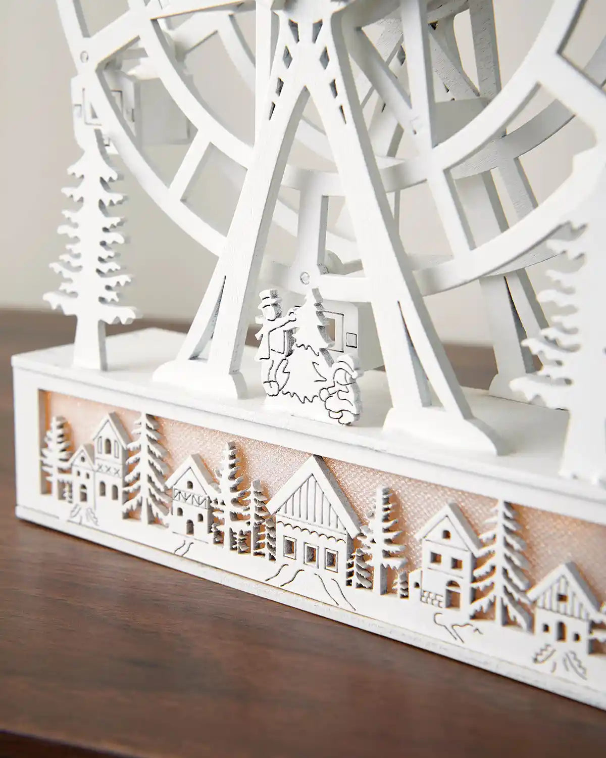 Close-up of pre-lit animated white ferris wheel base with warm white light on dark wood surface 