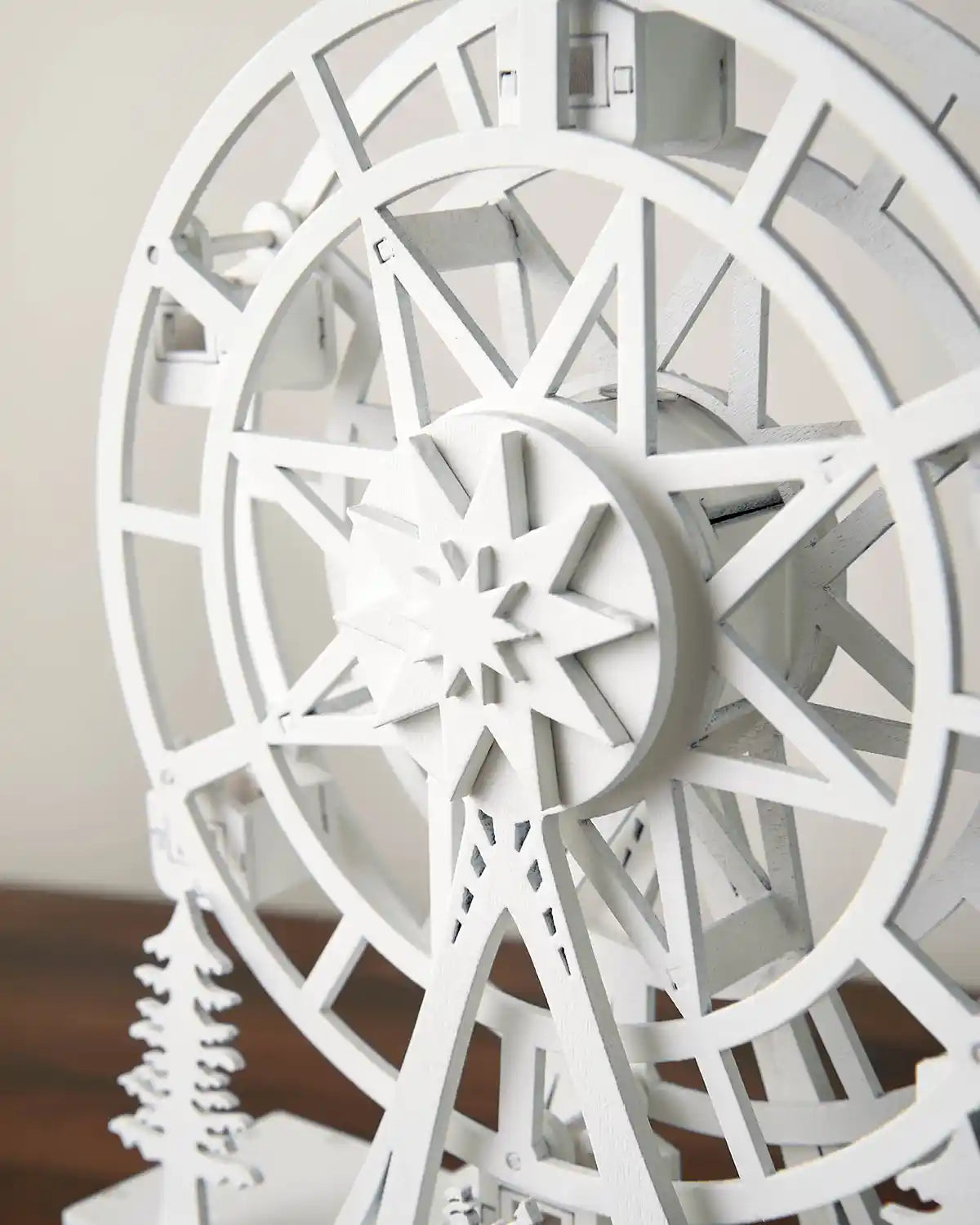 Close-up of body of pre-lit white animated ferris wheel on dark wood surface in front of white wall