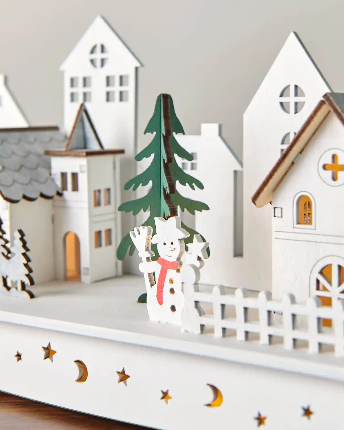Close-up of pre-lit white wooden village featuring snowman and buildings in warm white light