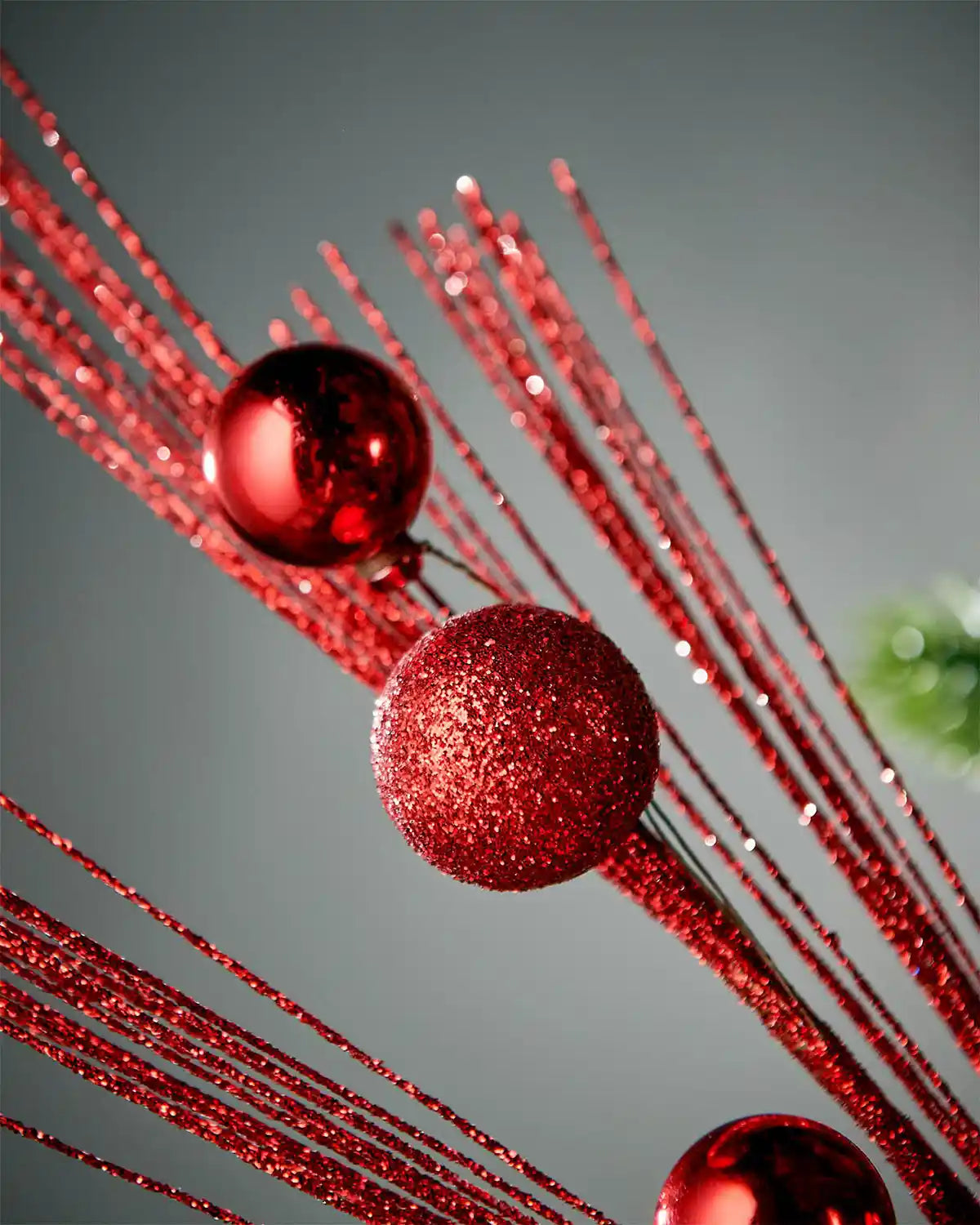Close-up of red glitter bauble spray with a focus on baubles in front of grey background