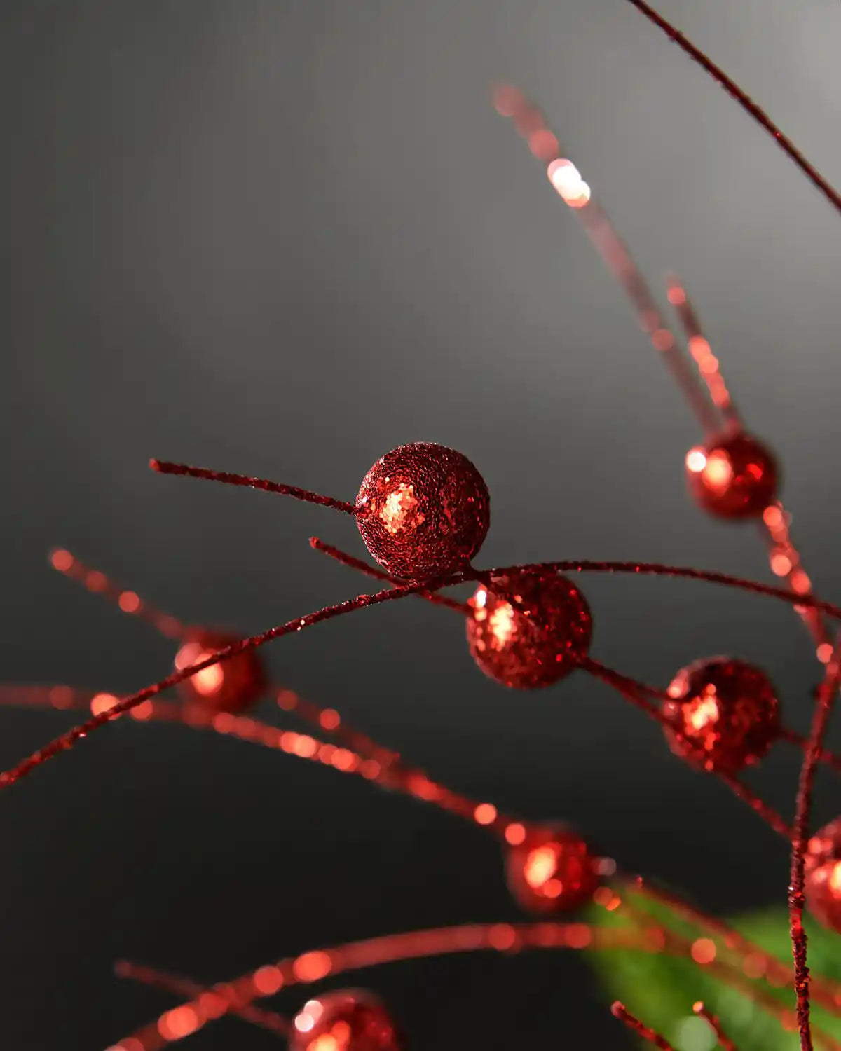 Close-up of red glitter berry spray in front of grey wall background highlighting berry glitter effect