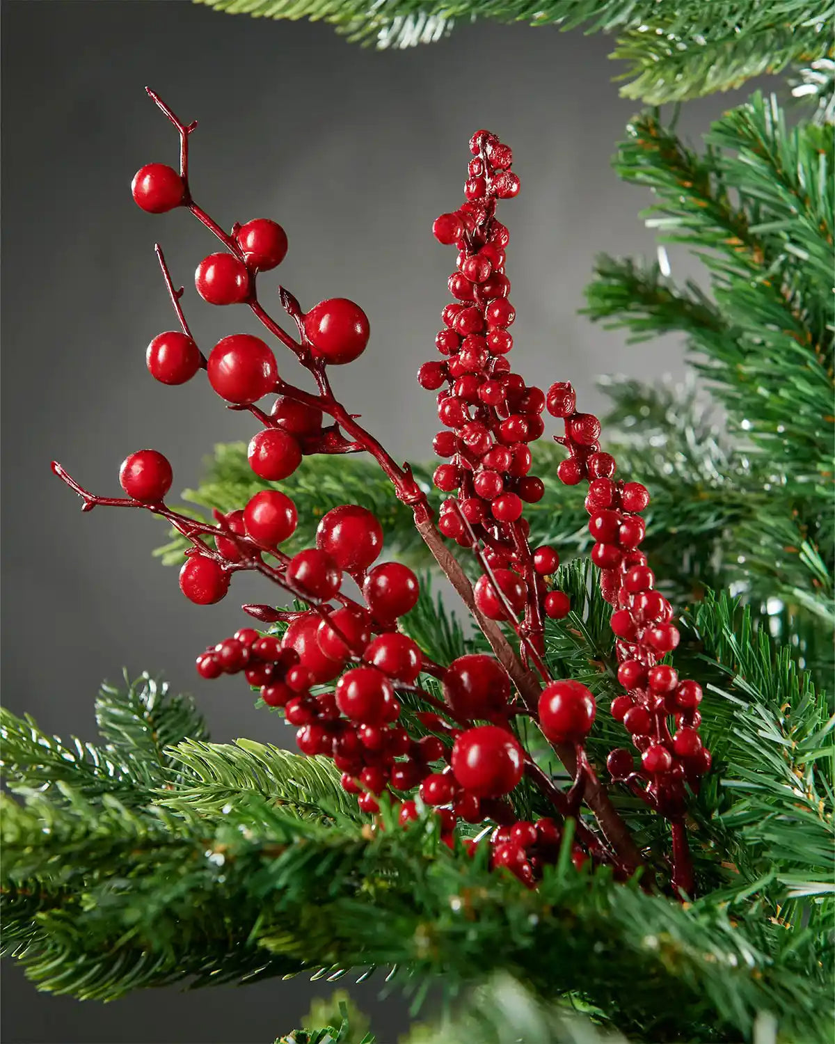 Close-up of red mixed berries spray attached to Christmas tree in front of grey wall background