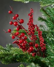 Close-up of red mixed berries spray attached to Christmas tree in front of grey wall background