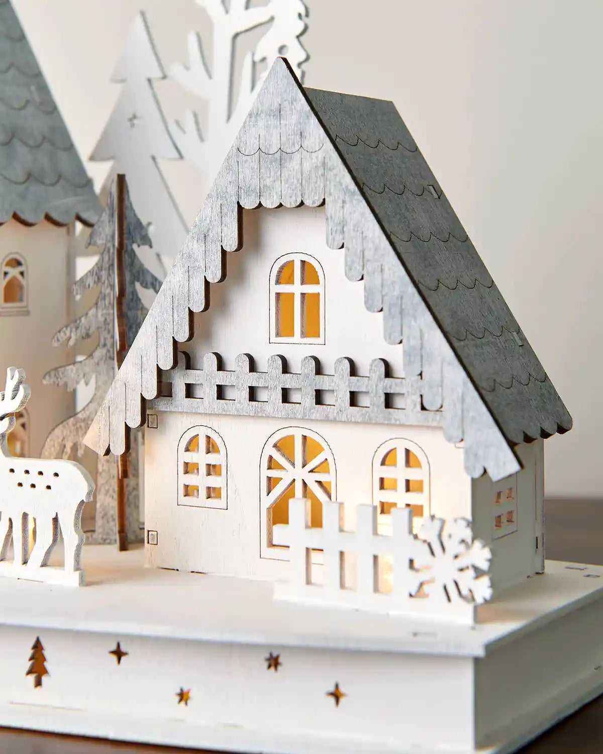 Close-up of right side of 40cm pre-lit white wooden village with warm white lighting on dark surface with white wall