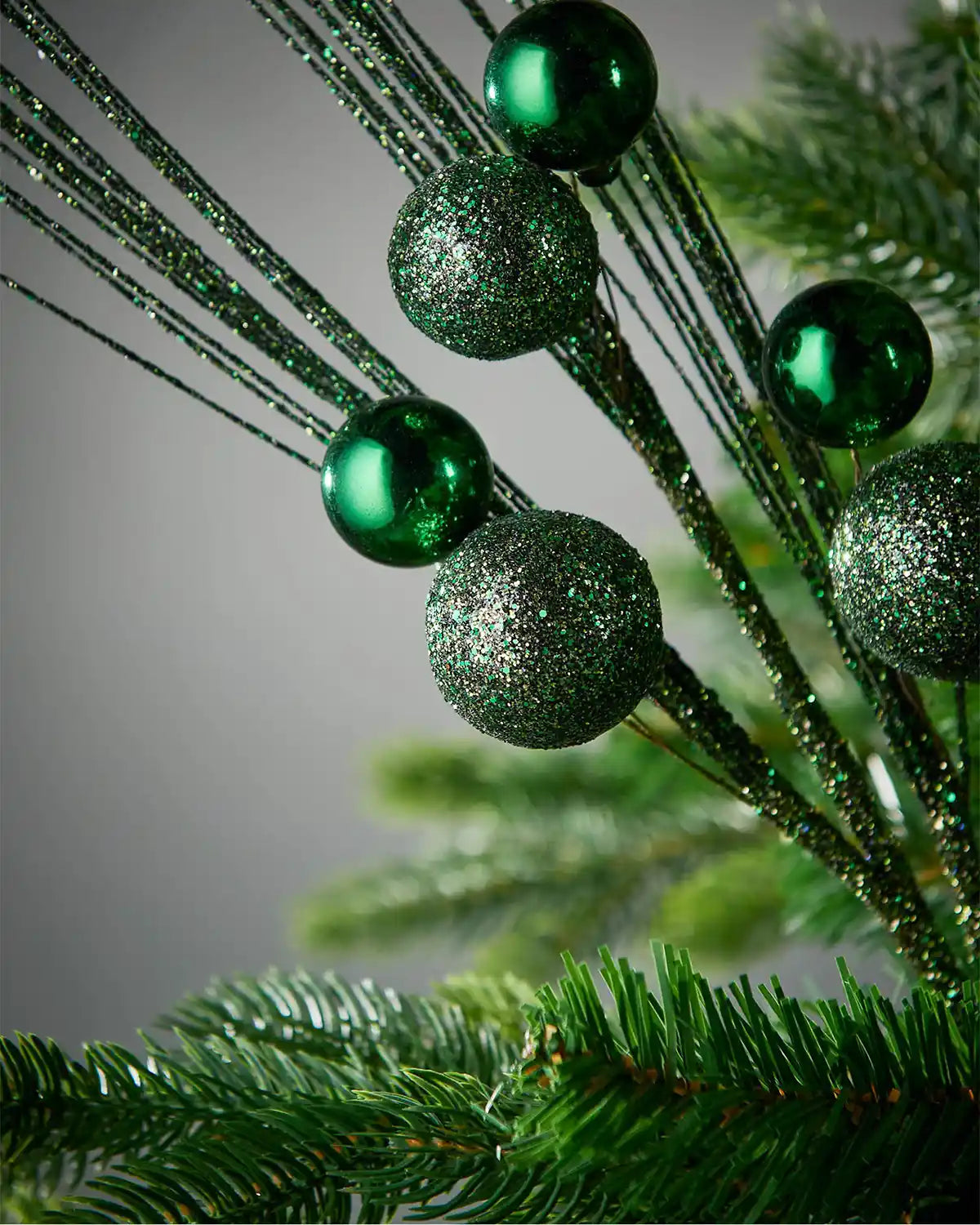 Close-up of sage green glitter bauble spray on Christmas tree highlighting baubles in front of grey background