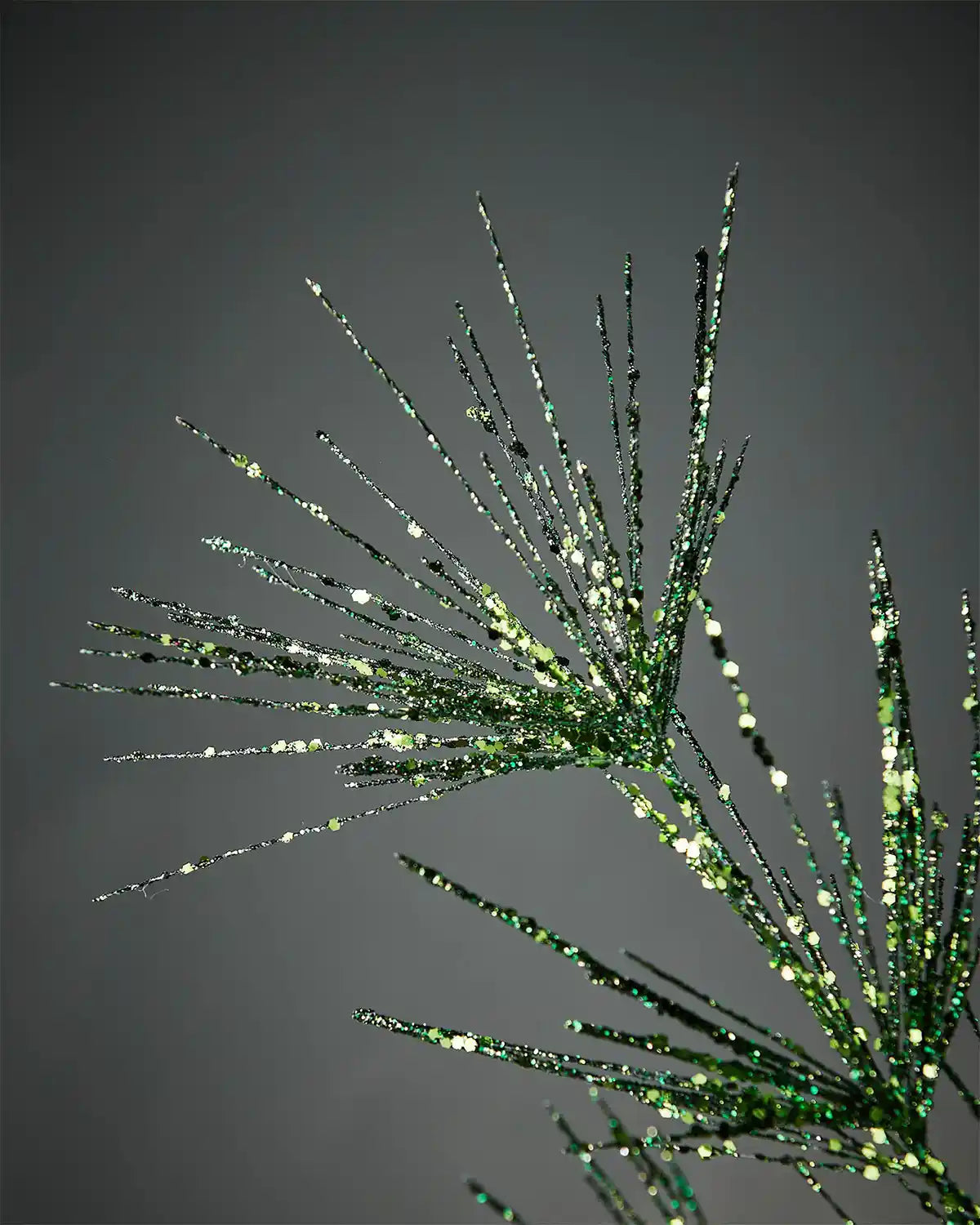 Close-up of sage green glitter firework spray in front of grey wall