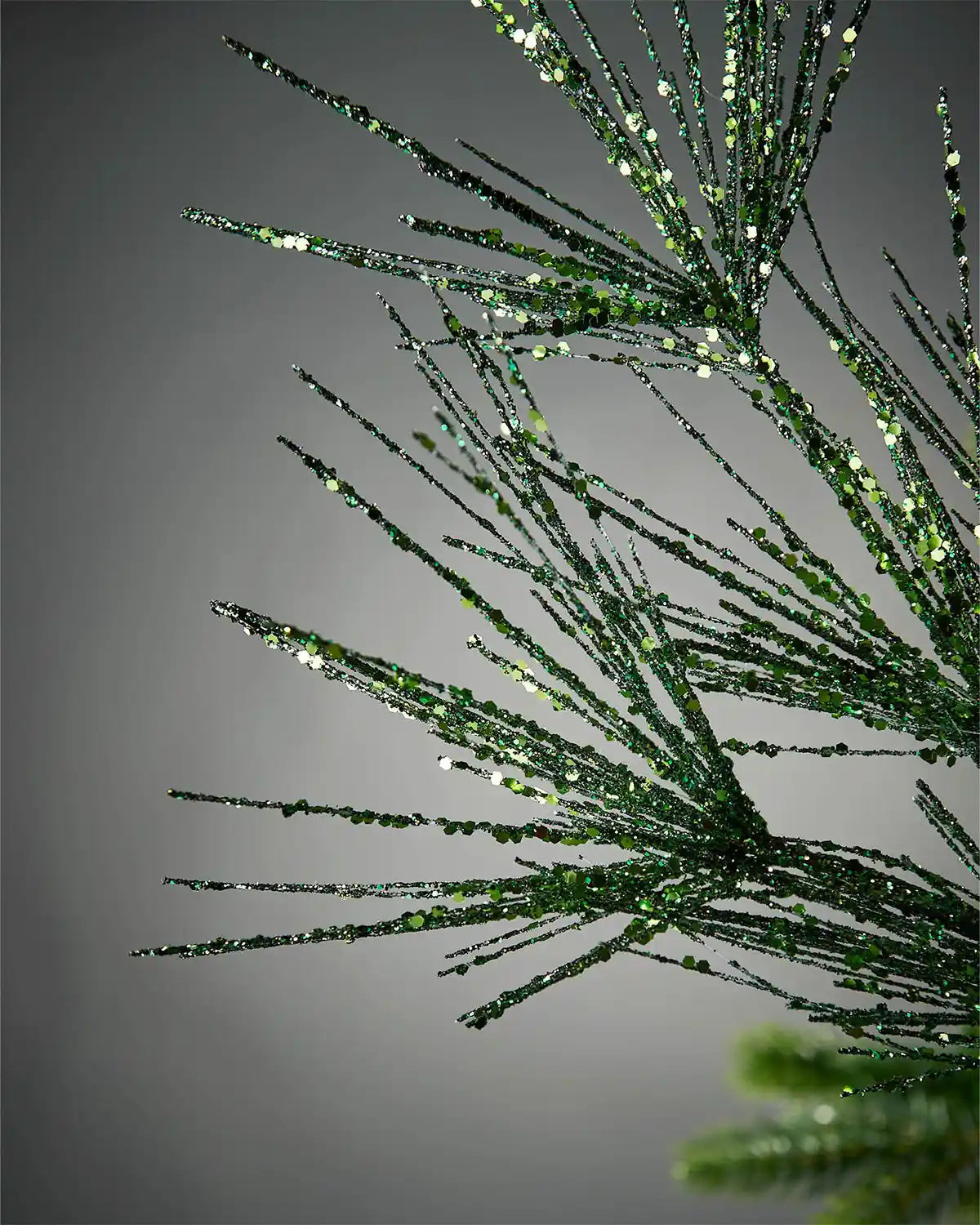 Close-up of sage green glitter firework spray in front of grey background highlighting sparkle