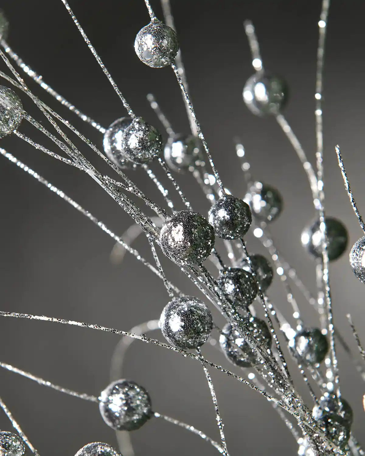 Close-up of silver berries spray in front of grey wall background highlighting glitter effect