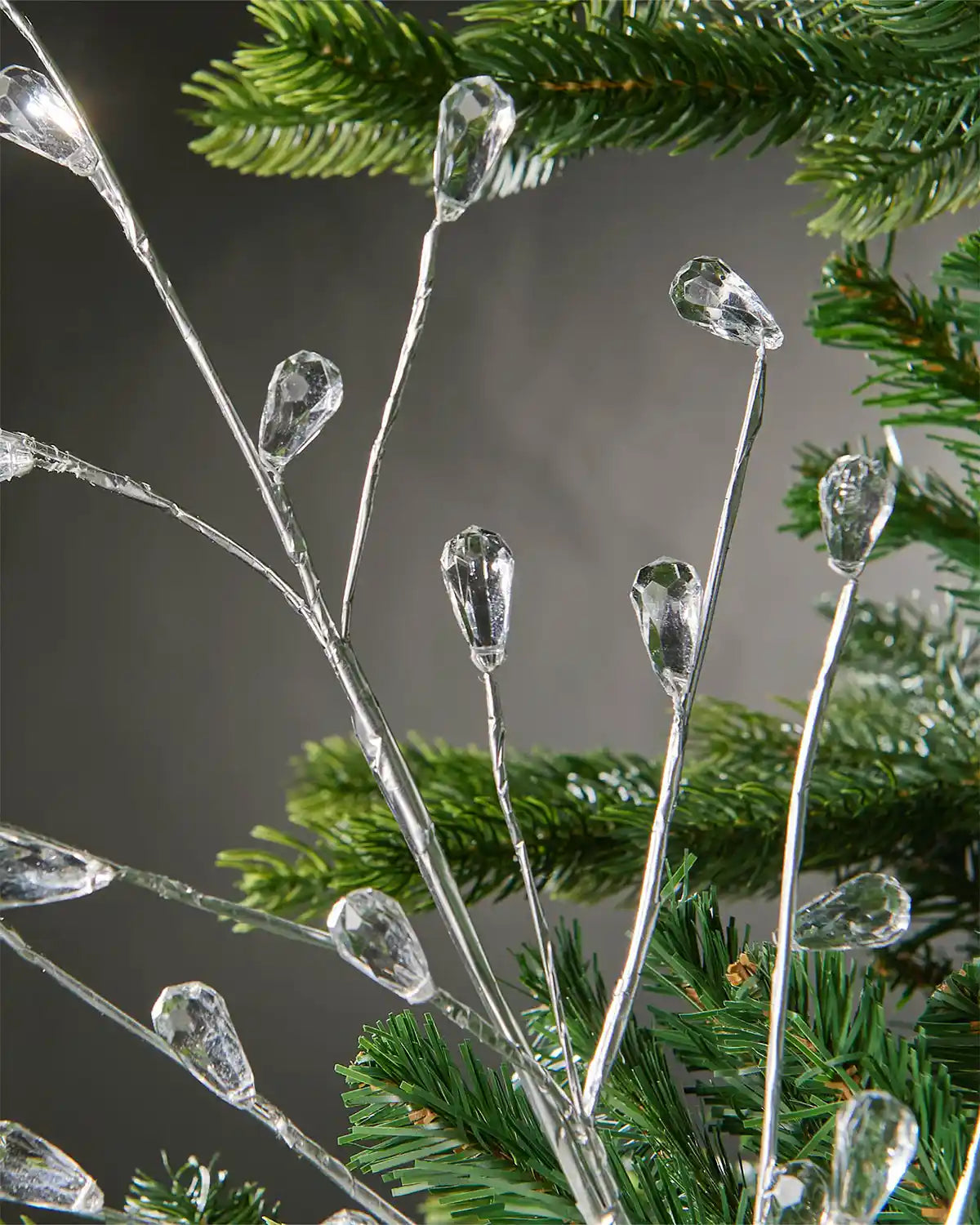 Close-up of silver crystal teardrop spray attached to Christmas tree in front of grey wall background