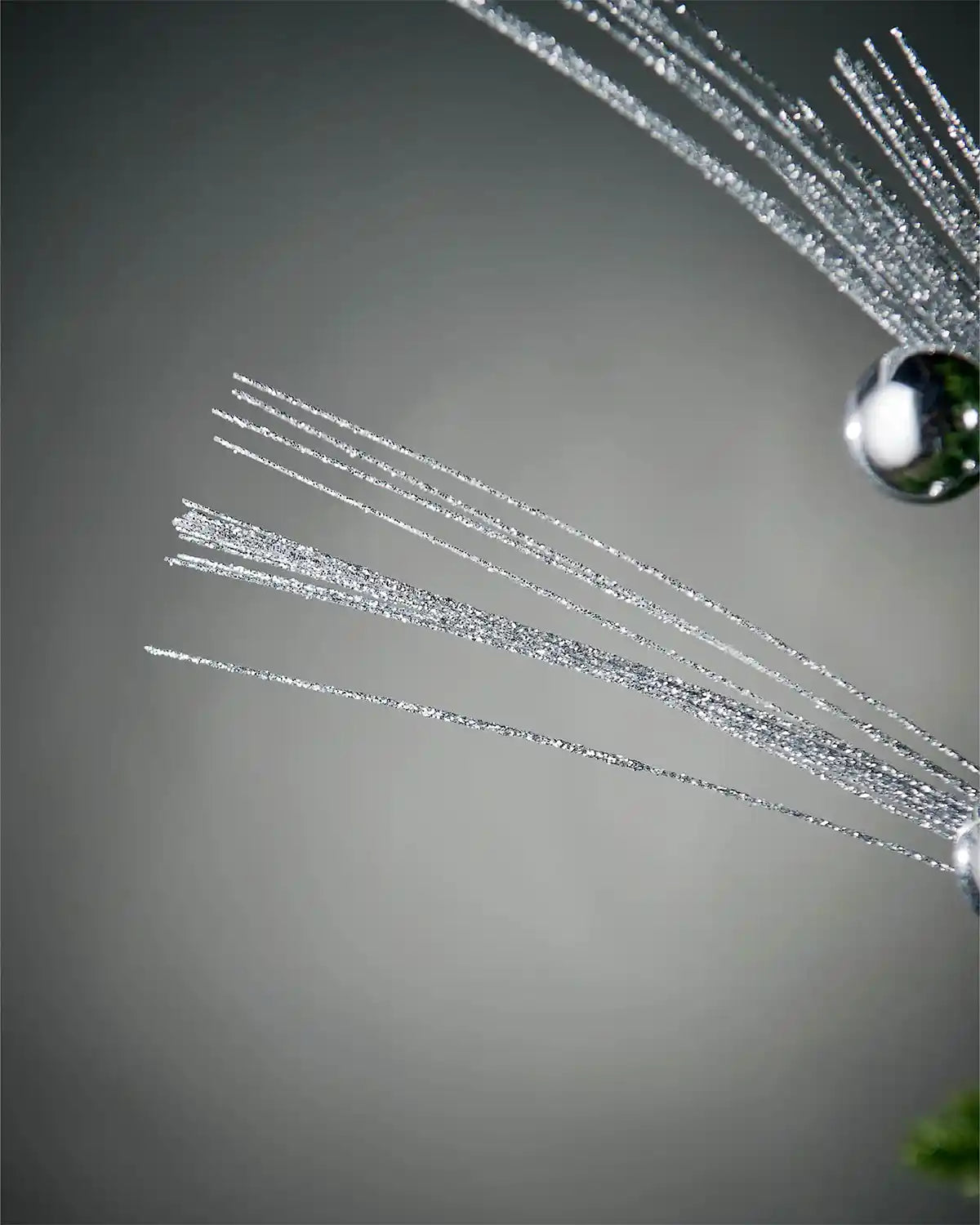 Close-up of foliage part of silver glitter bauble spray in front of grey background