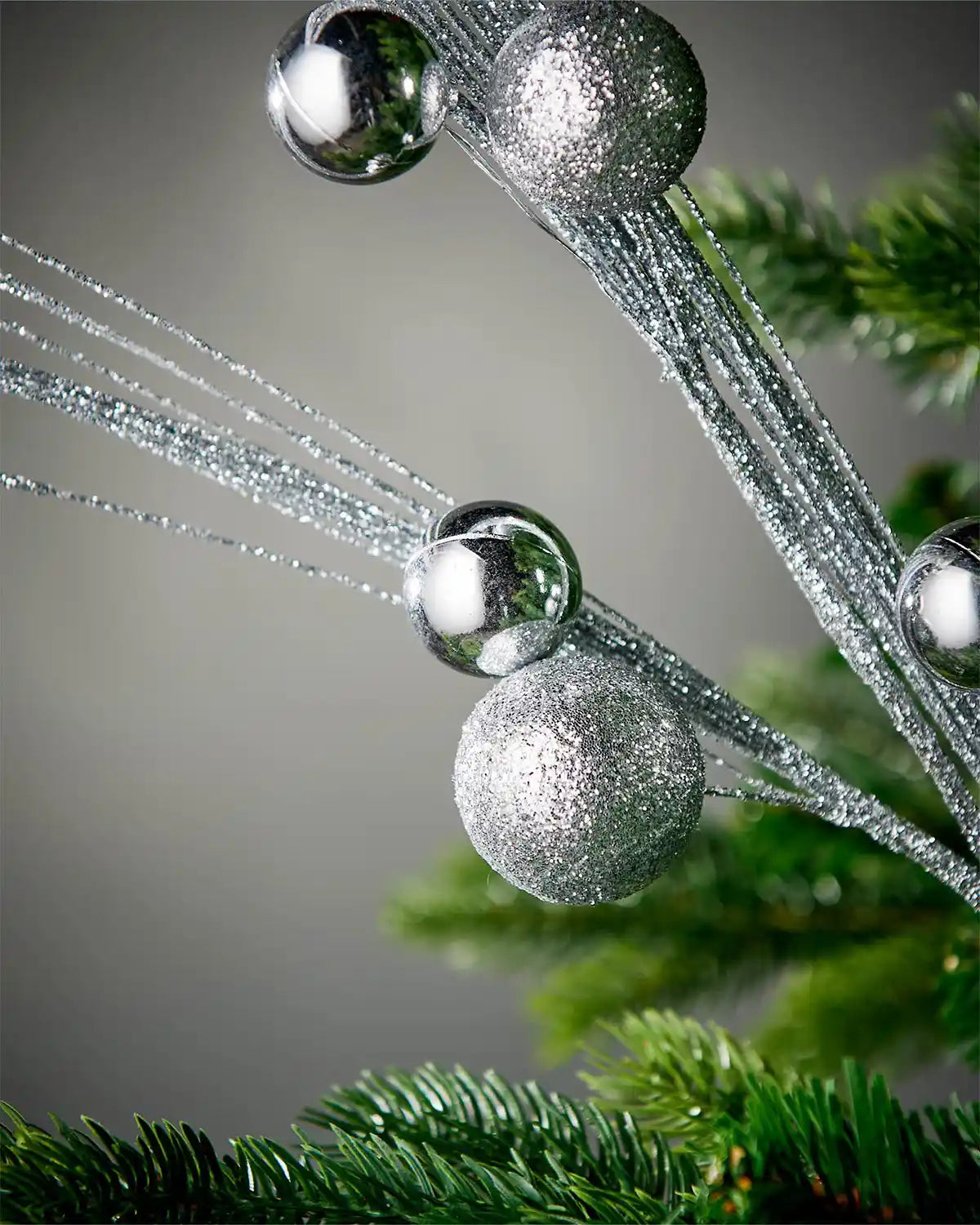 Close-up of silver glitter bauble spray inside tree in front of grey background