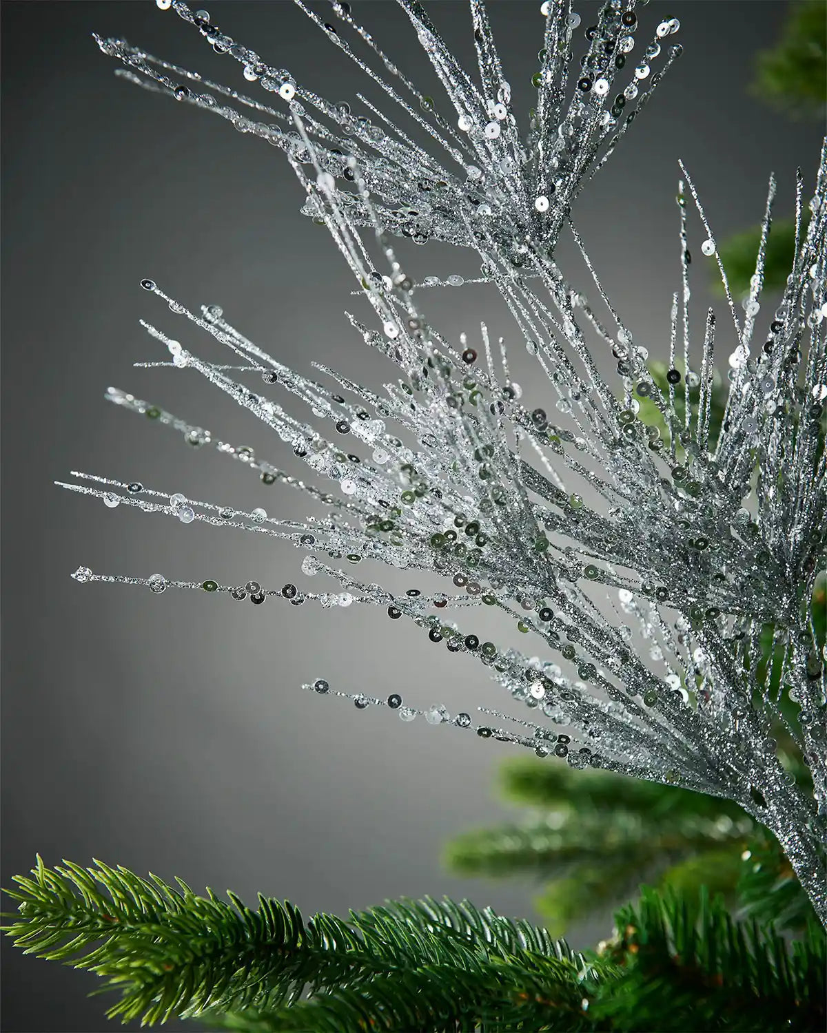 Close-up of silver glitter firework spray in Christmas tree highlighting sequin detail in front of grey background