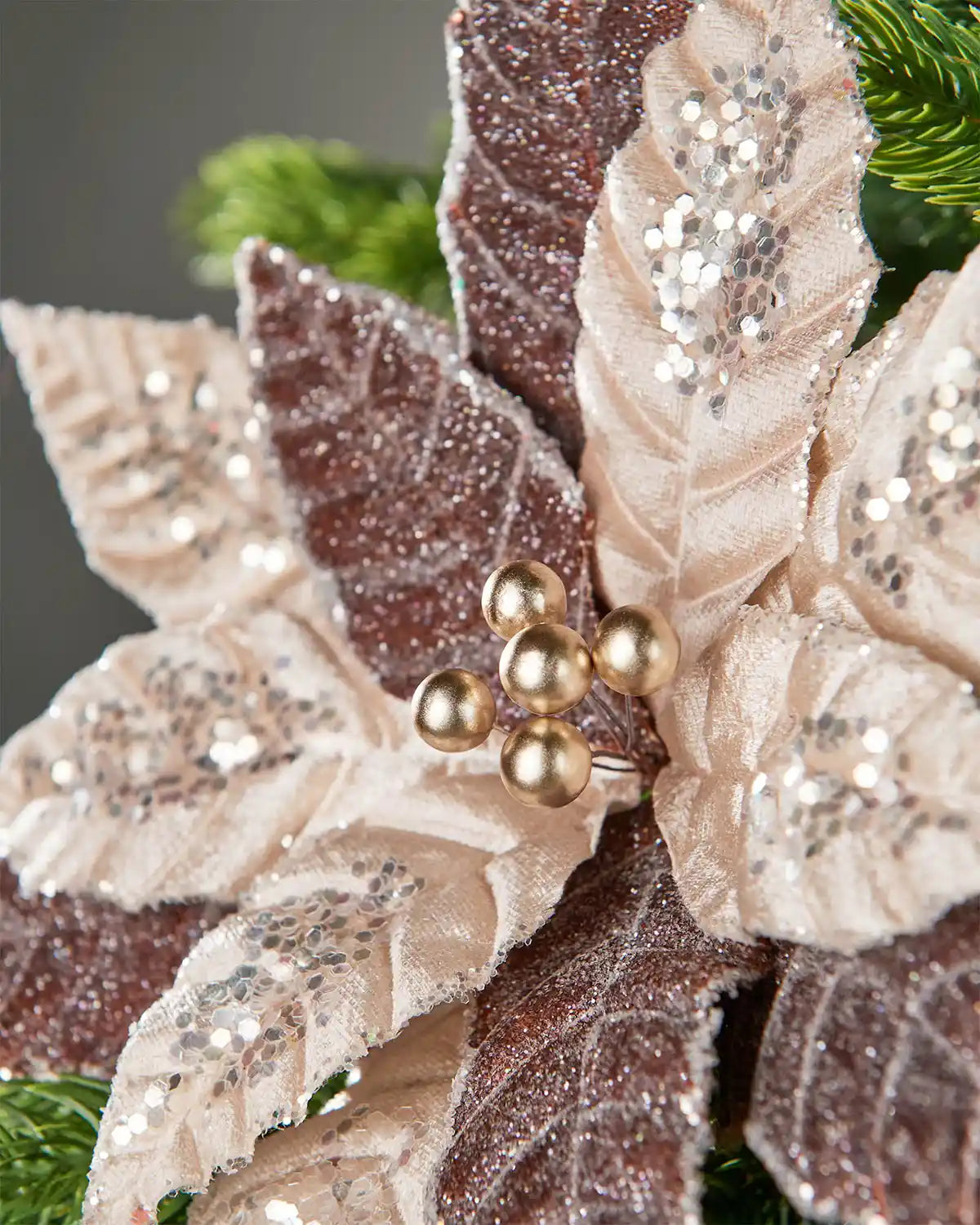 Close-up image of two-tone brown and beige glitter artificial poinsettia flower decoration attached to Christmas tree in front of grey wall background