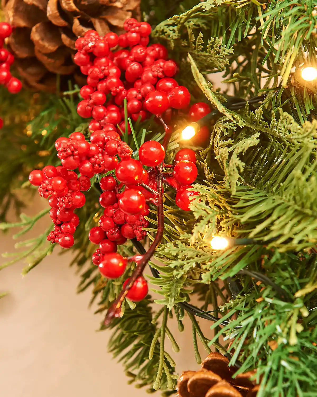 Close up view Christmas wreath with red berries, warm white LED lights on a light background
