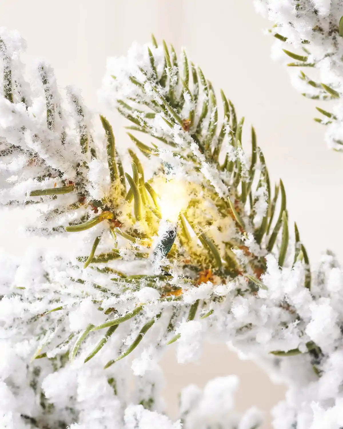 Close up view of a Snow Flocked Potted Christmas Tree PVC and PE tips with a single lit bulb against a cream wall