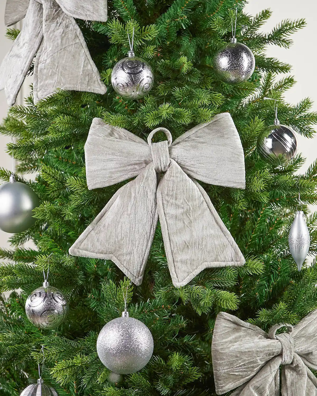 Close-up of vintage-style silver velvet bow attached to a Christmas tree surrounded by additional bows and silver baubles