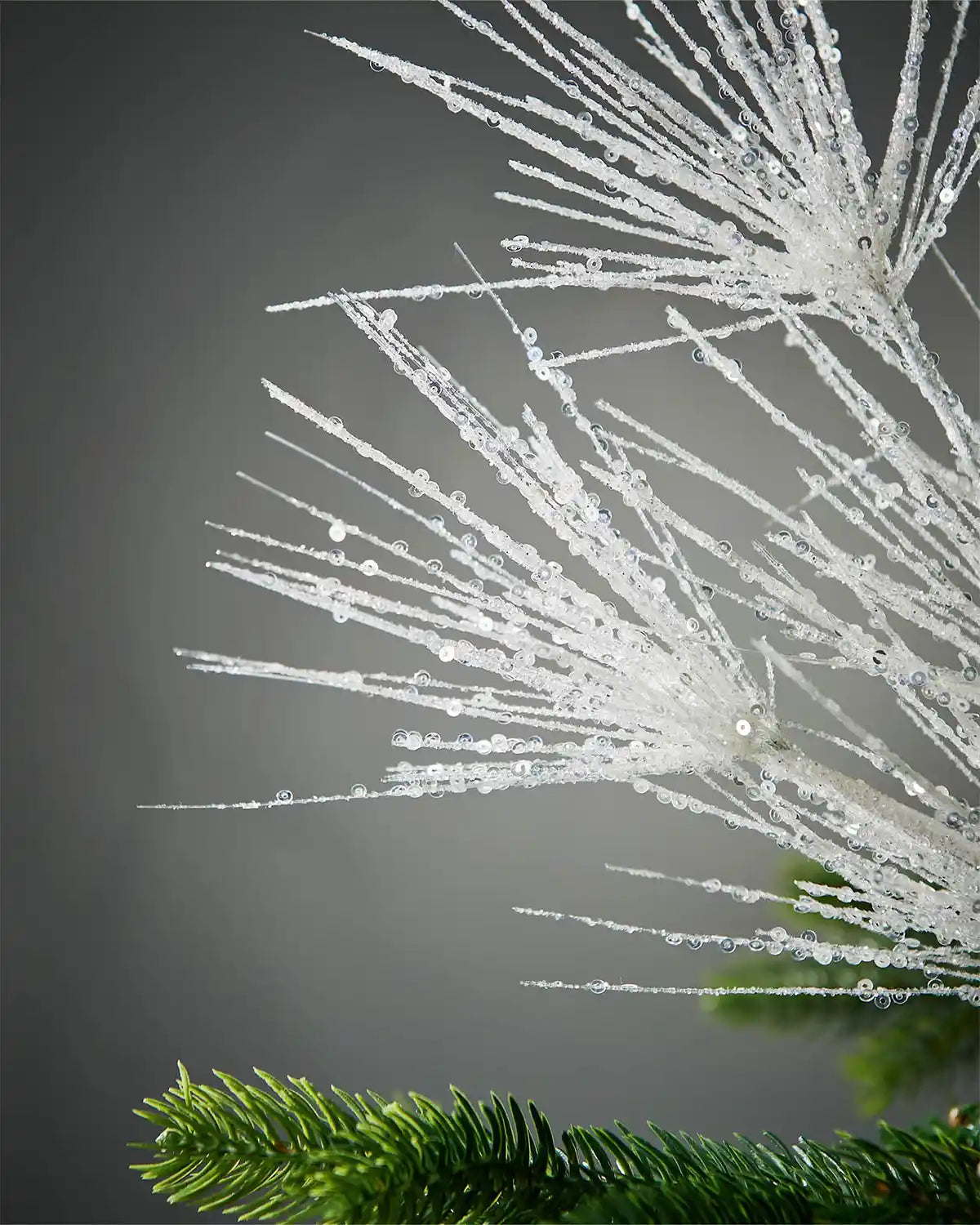 Close-up of sequin foliage on white glitter firework spray on tree in front of grey background