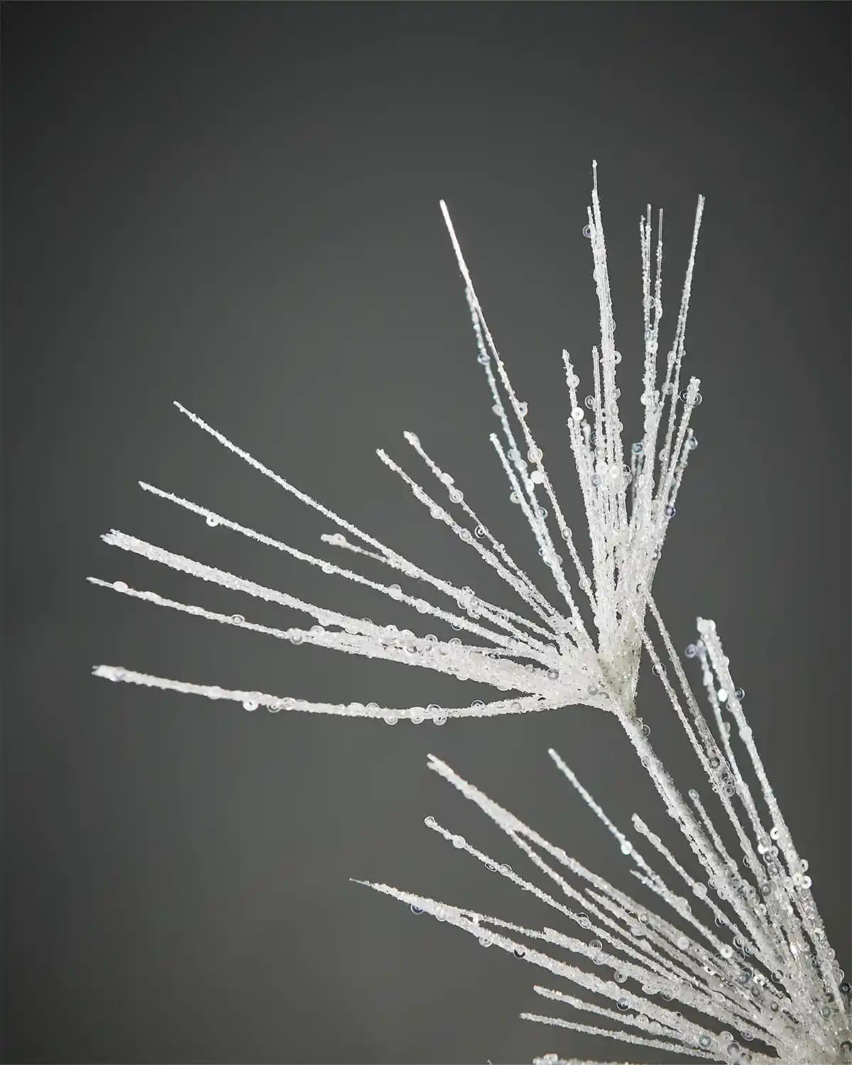 Close-up of white glitter firework spray in front of grey background showcasing sequin details