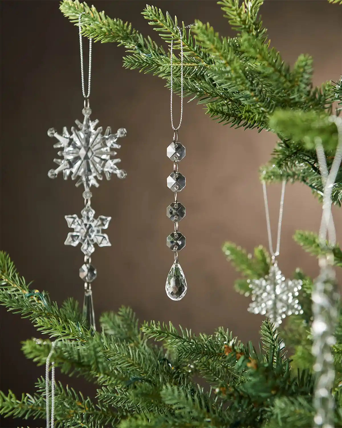 Crystal snowflake ornaments hanging on a Christmas tree with a brown background