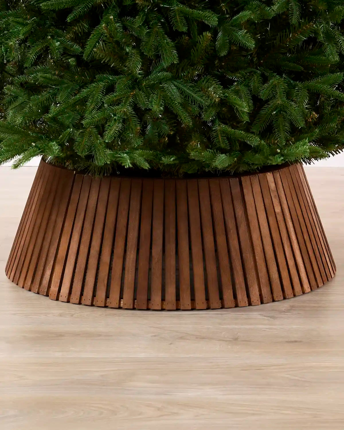 Dark brown wooden slat tree collar under a Christmas tree on a wooden floor
