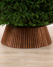 Dark brown wooden slat tree collar under a Christmas tree on a wooden floor