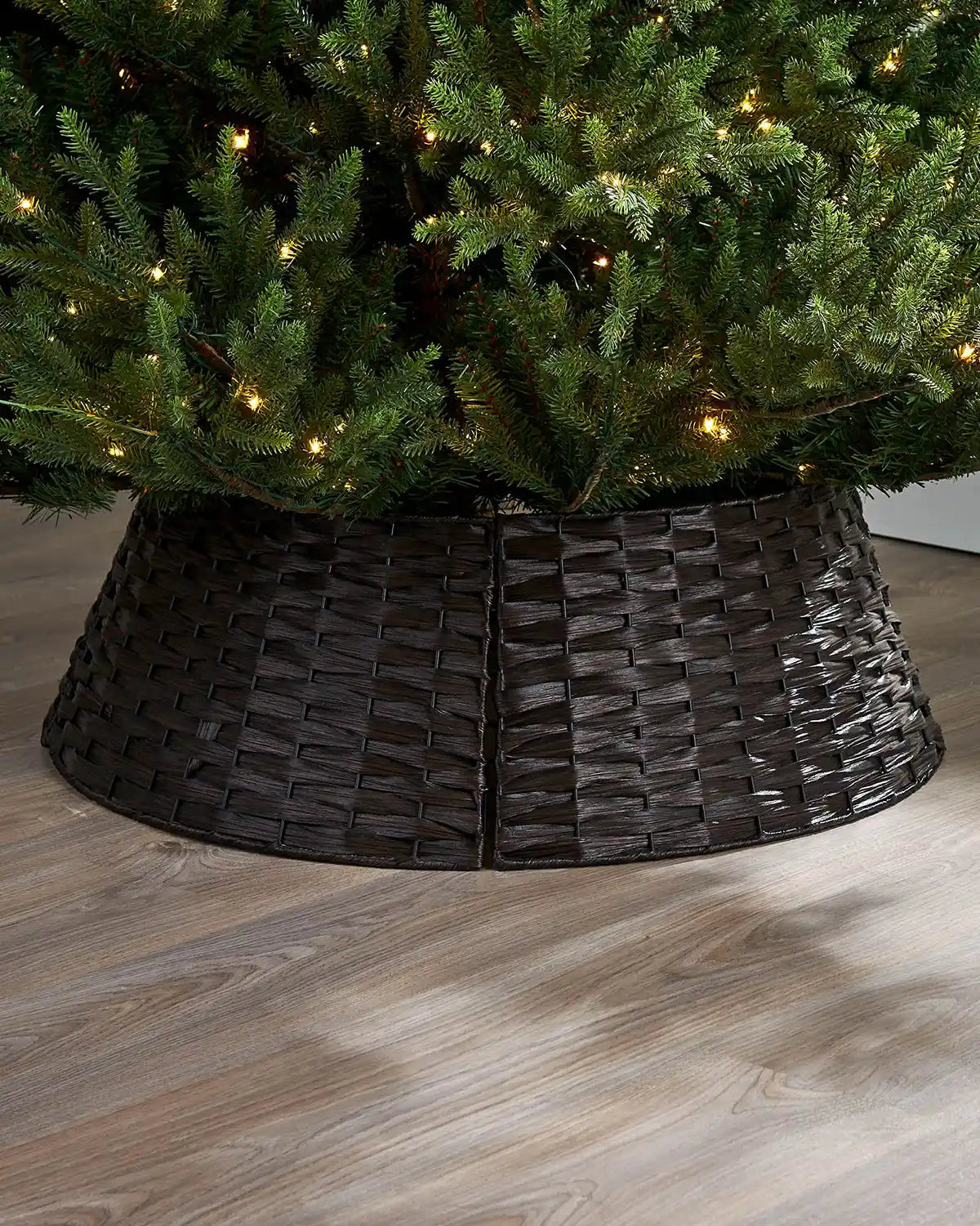 Dark brown woven tree collar around a decorated Christmas tree on a wooden floor.