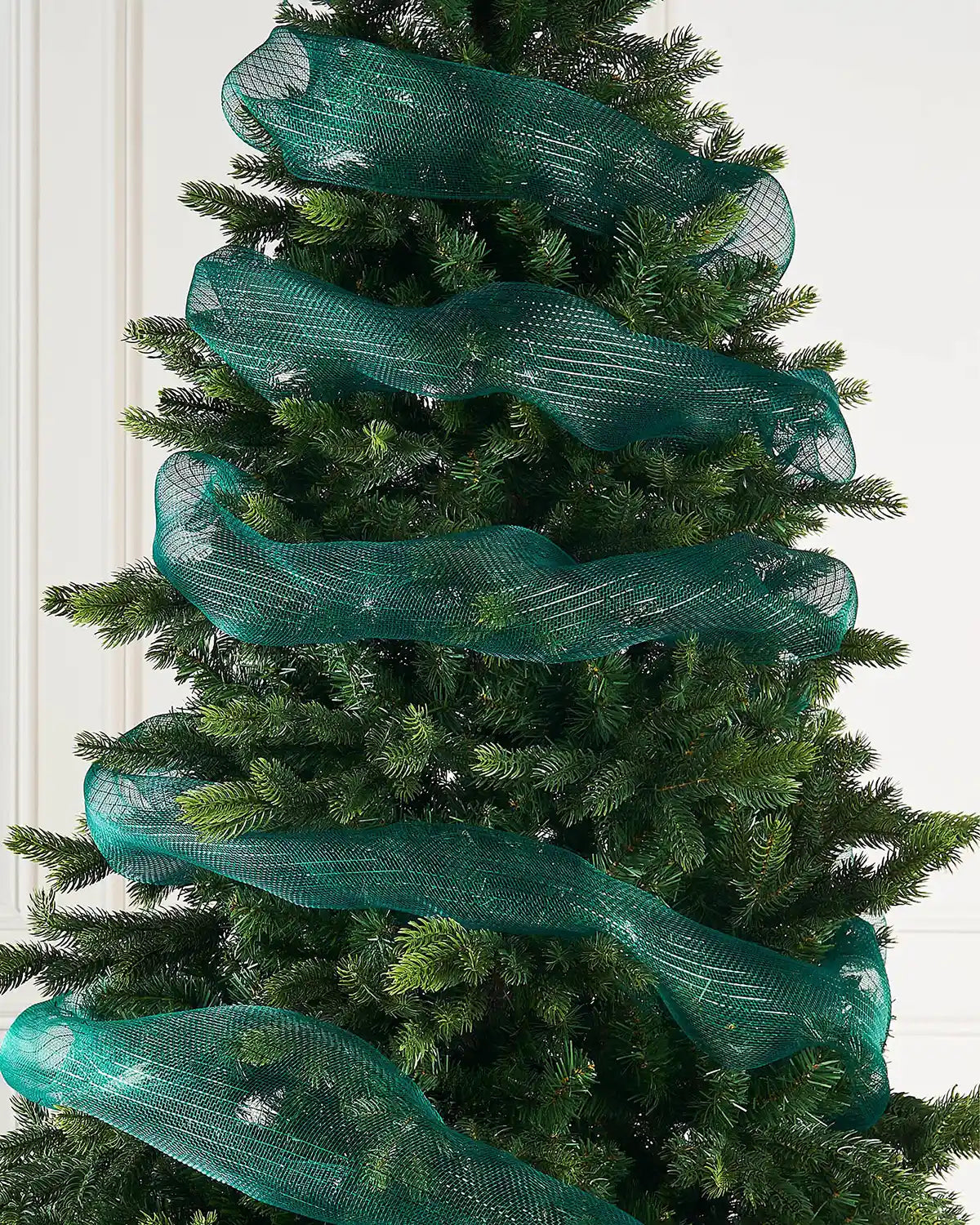 Dark green mesh ribbon wrapped around Christmas tree against a cream panel background 
